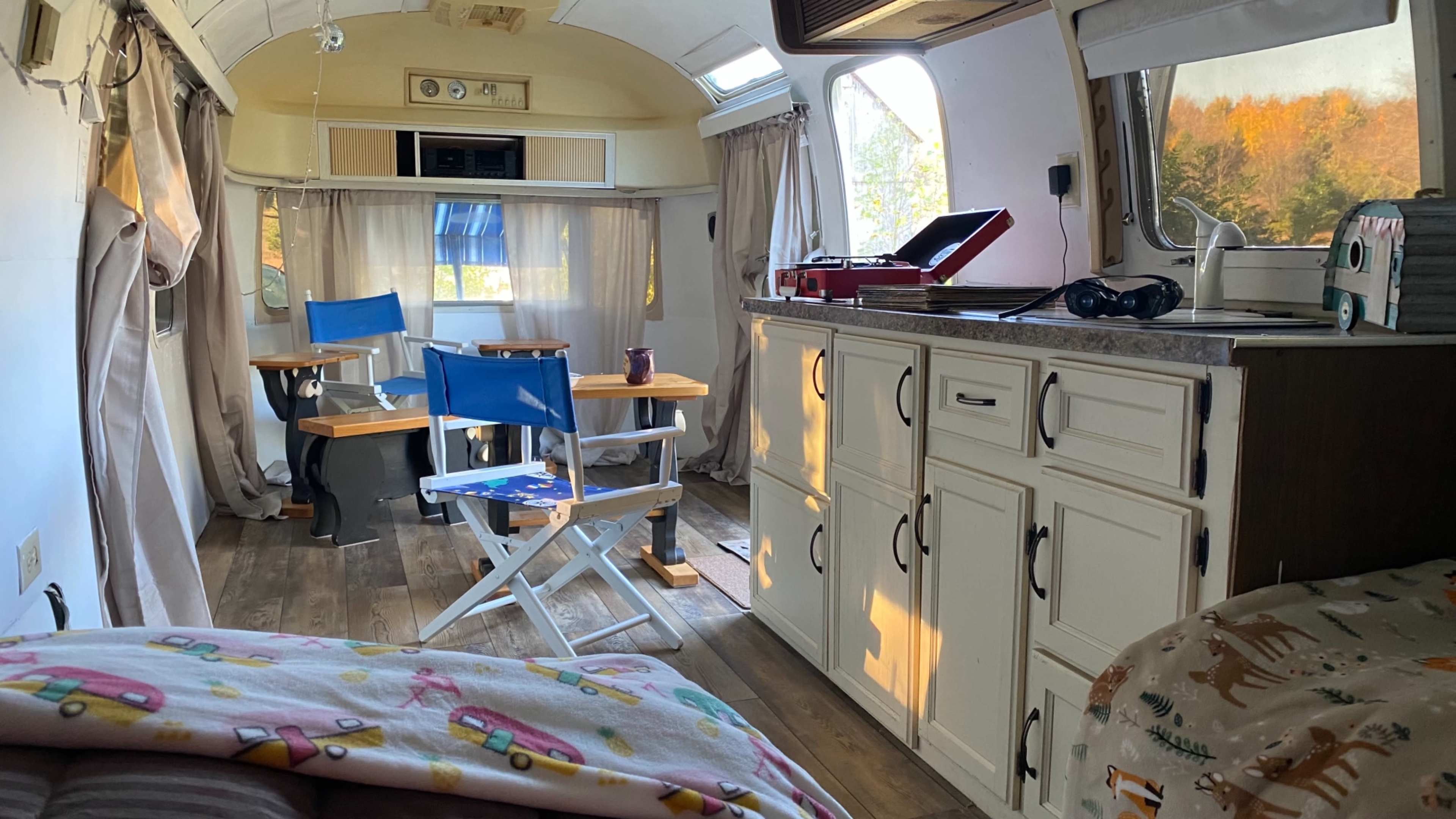 The interior of a camper with a kitchen area, dining space, and two blue folding chairs, illuminated by natural light coming through the windows.