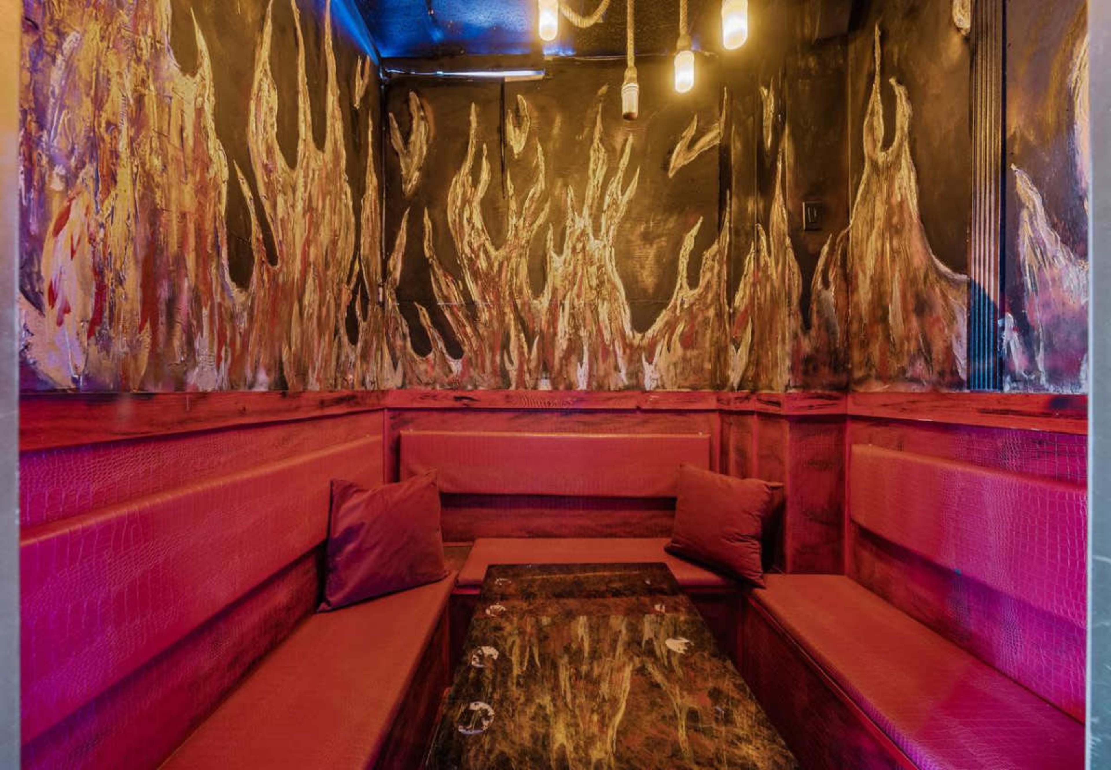 The image shows a small seating area with red upholstered benches and a dark, flame-themed mural on the walls illuminated by pendant lights.