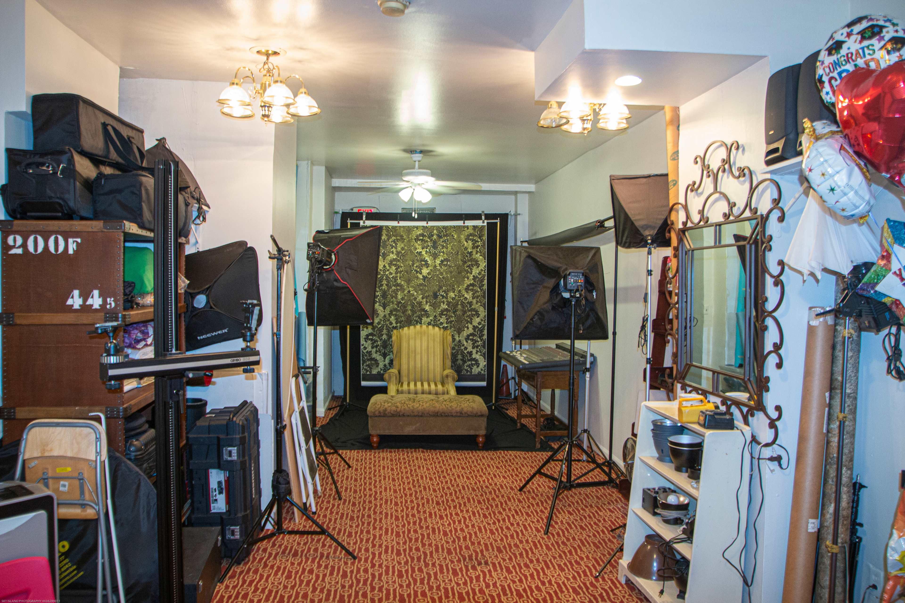 A photo studio setup with a decorative backdrop, lighting equipment, and a throne-like chair in the center.