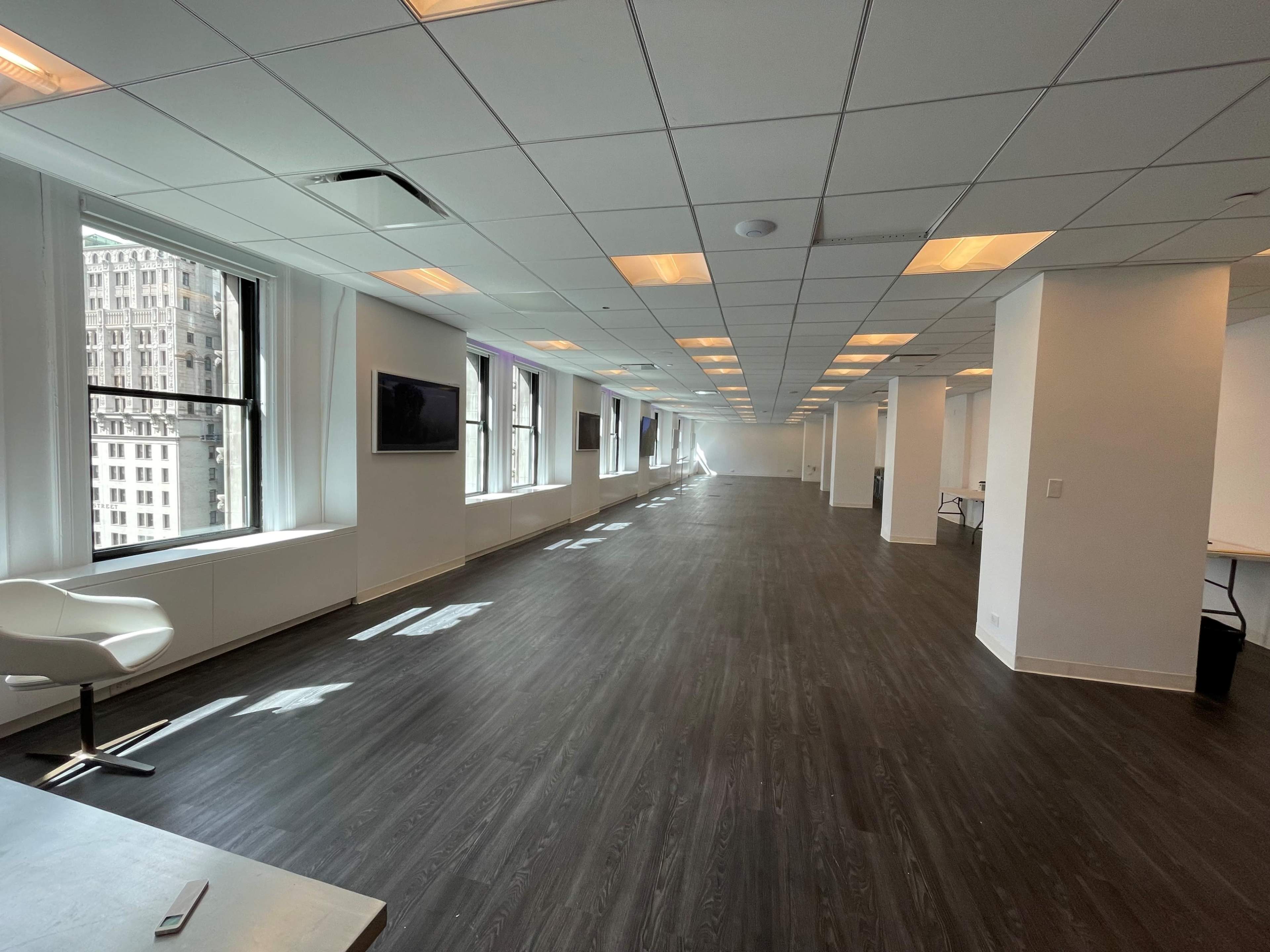 A spacious, modern office interior with large windows and polished wooden flooring.