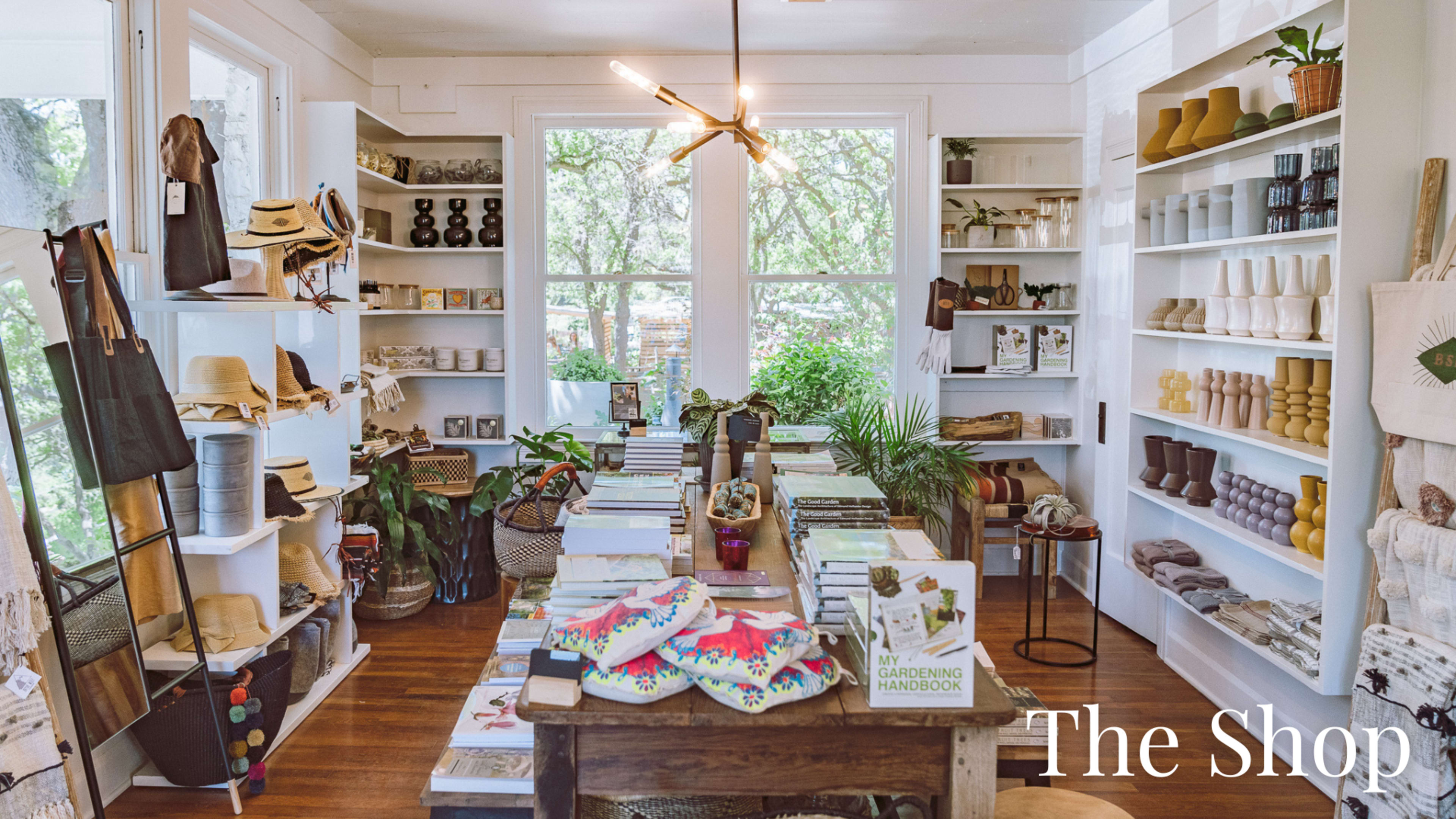 The image shows a well-organized shop interior featuring shelves filled with gardening supplies, books, and various decorative items.