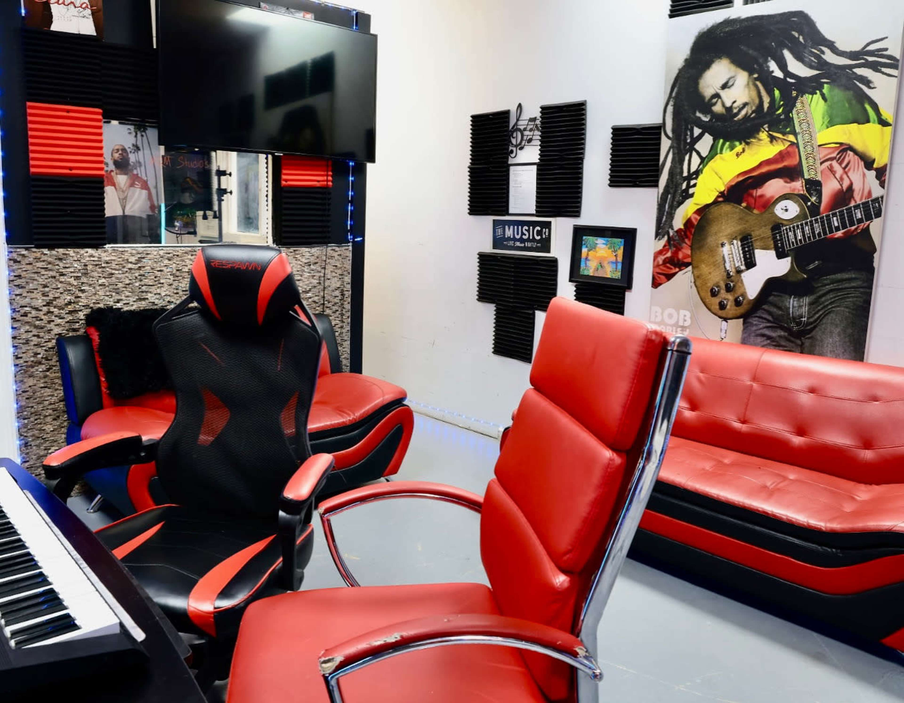 The image shows a recording studio with red and black furniture, including a gaming chair and a couch, decorated with a mural of Bob Marley on the wall.