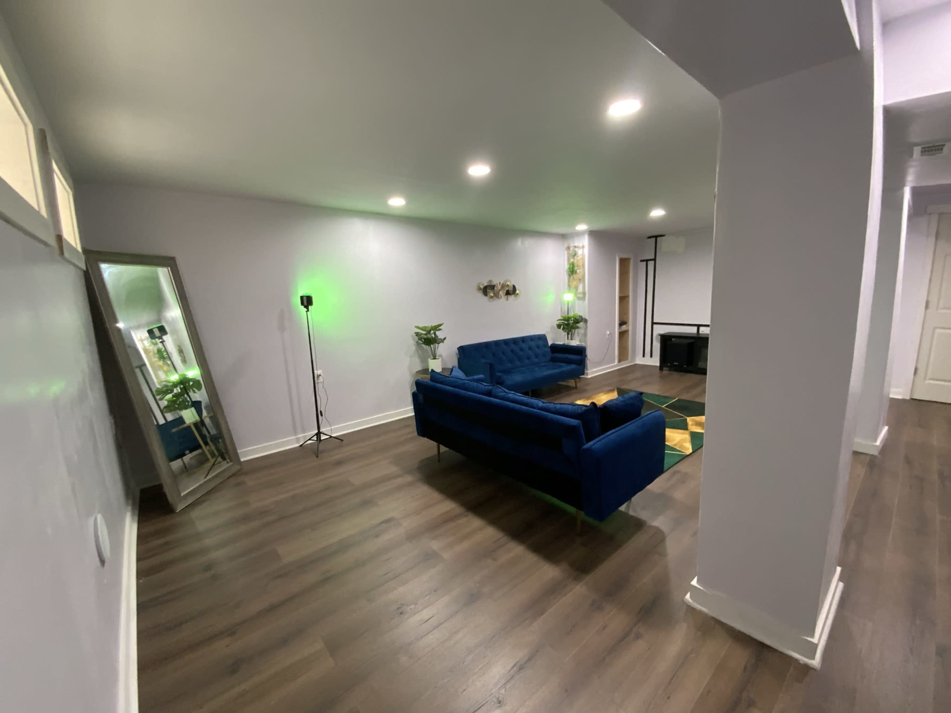 A spacious living room featuring a blue sofa, a large mirror, and a fireplace, with green lighting illuminating the walls.