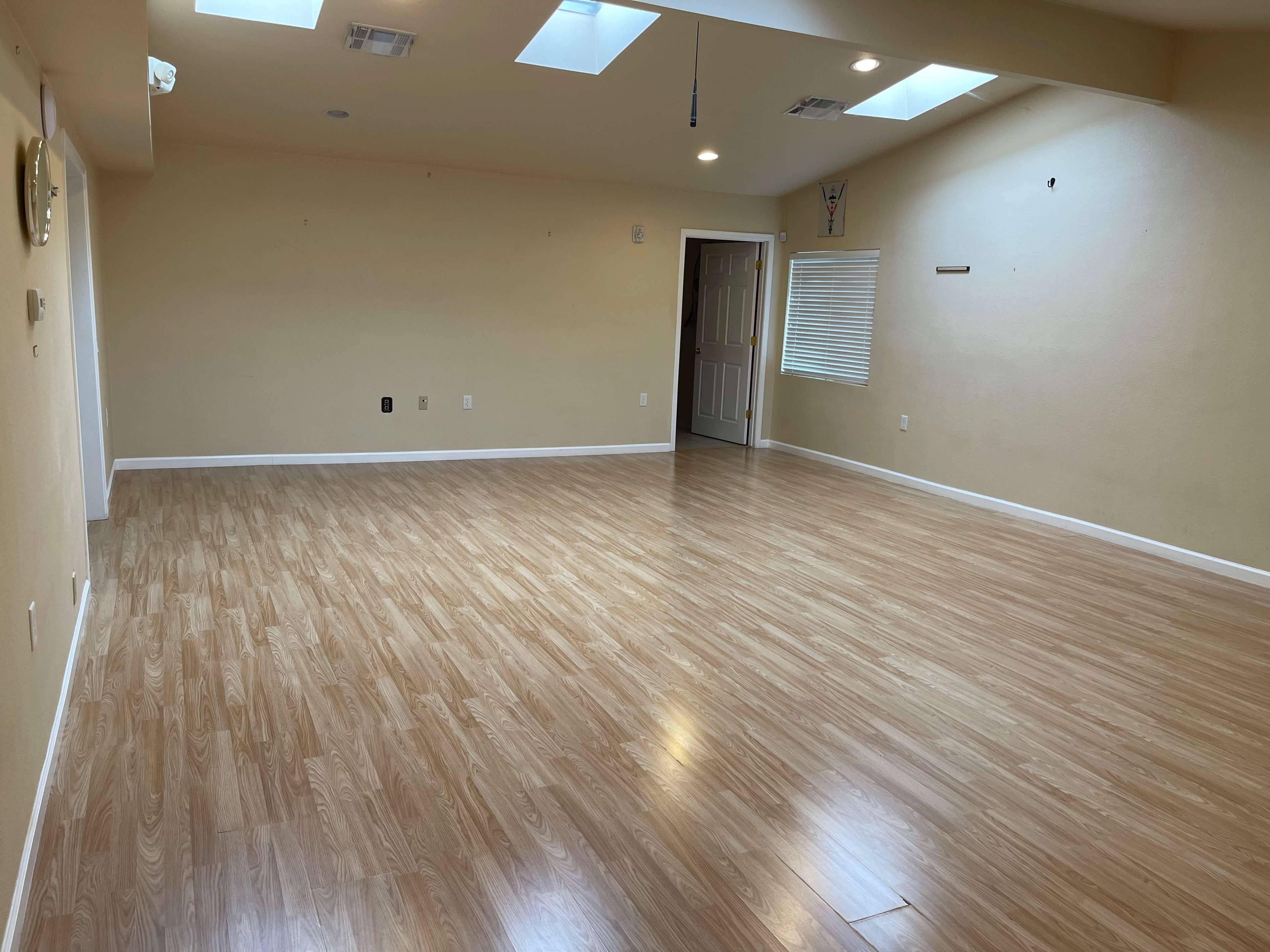 A spacious room with wooden flooring, skylights, and a closed door on one side.