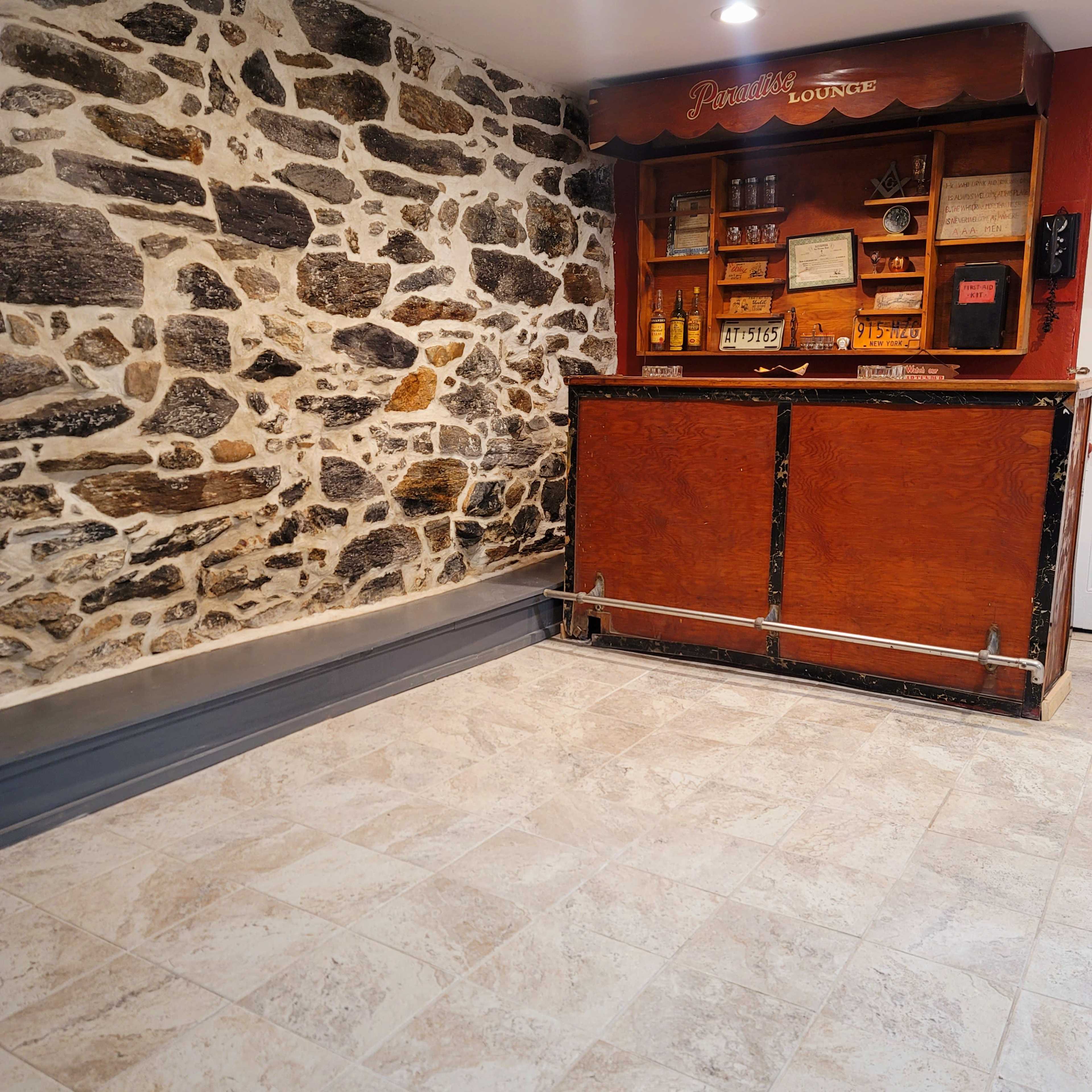 A lounge area with a stone wall, a wooden bar counter, and shelves displaying various bottles and framed items.