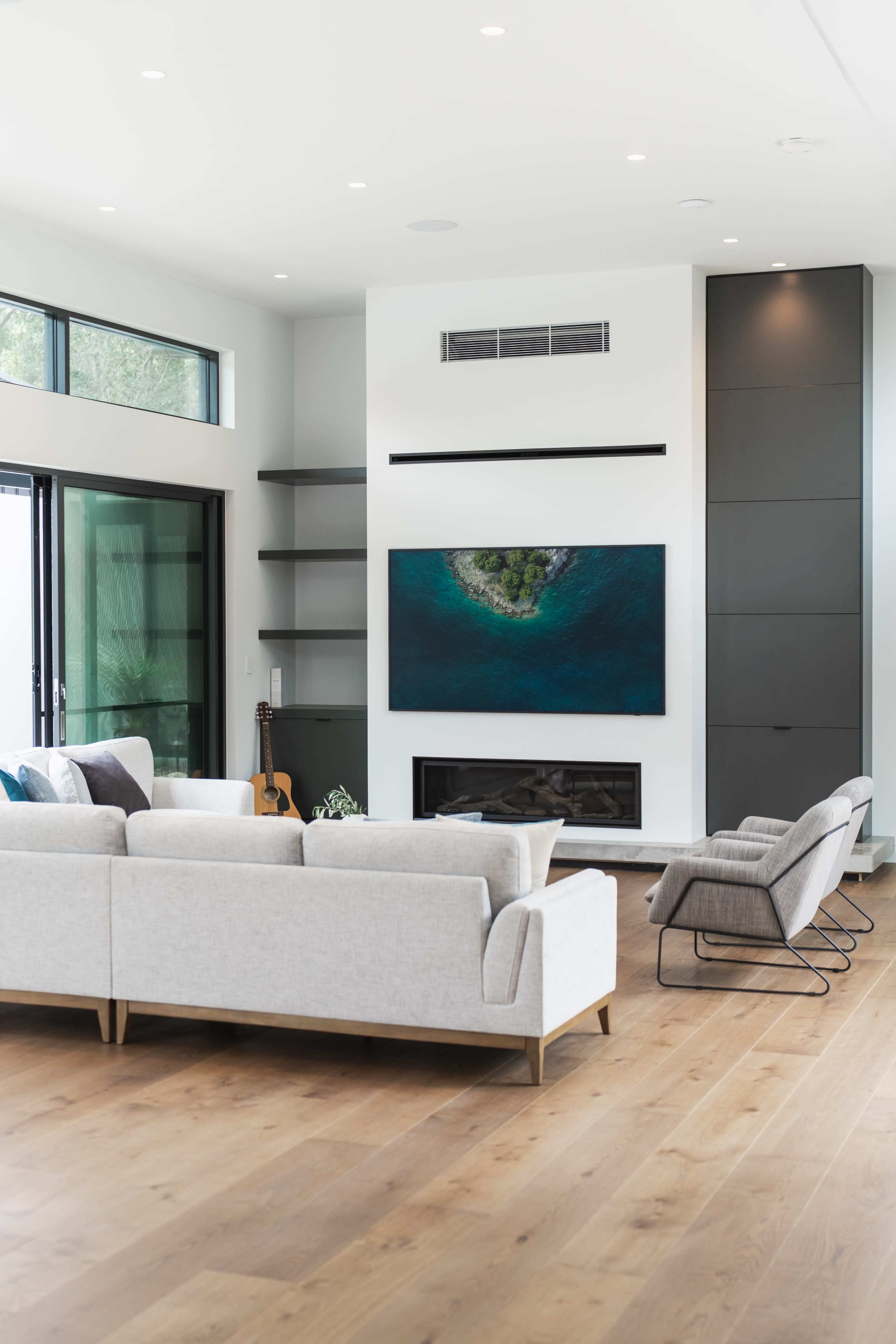 A modern living room features a gray sectional sofa, a sleek fireplace, and a large television mounted on the wall.
