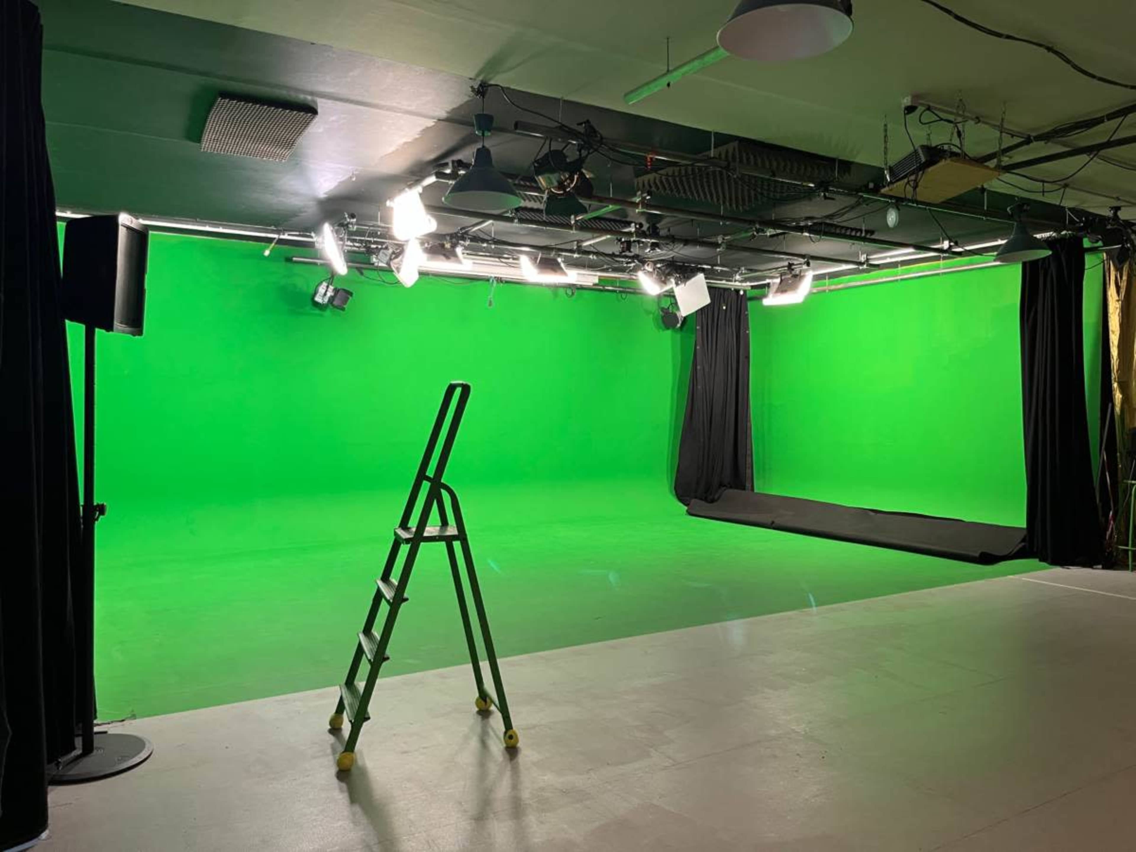 The image shows a green screen studio with a ladder and various lighting equipment arranged in the space.