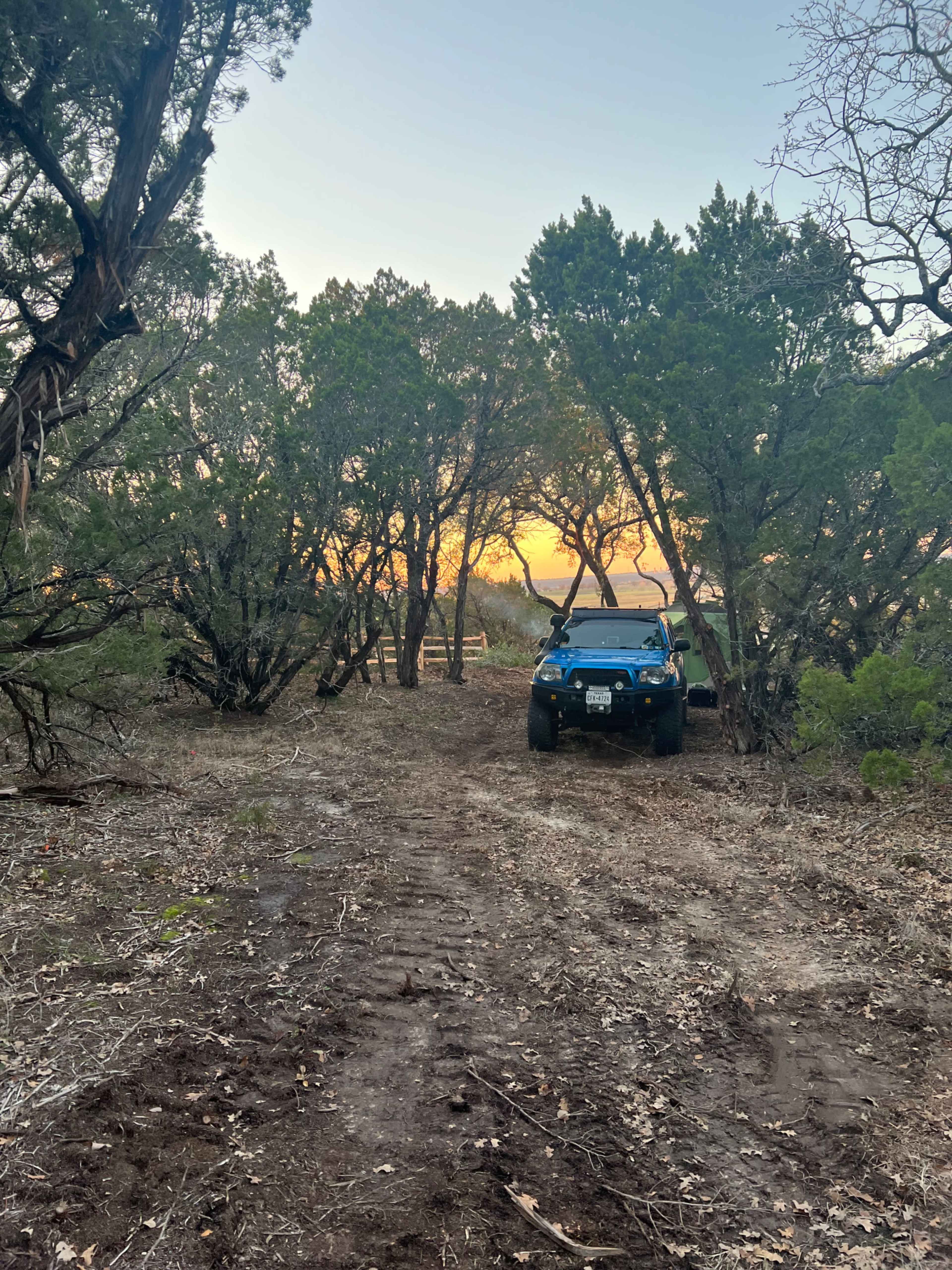 A blue all-terrain vehicle sits on a dirt path surrounded by trees as the sun sets in the background.