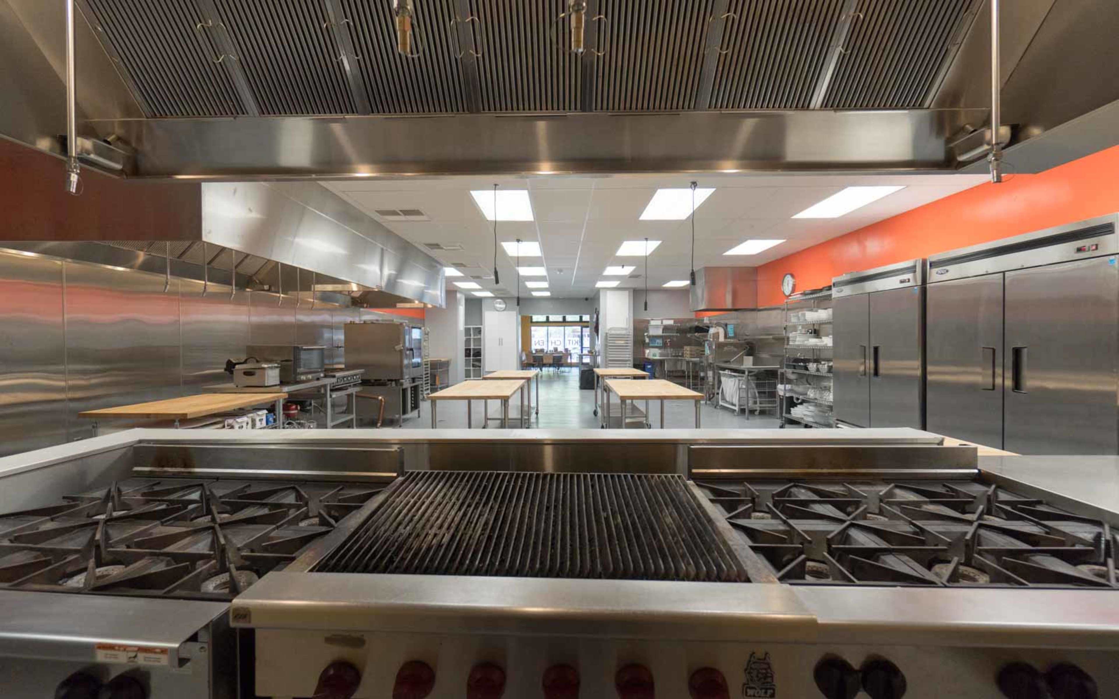 A spacious commercial kitchen with stainless steel appliances, multiple cooking stations, and large refrigerators.