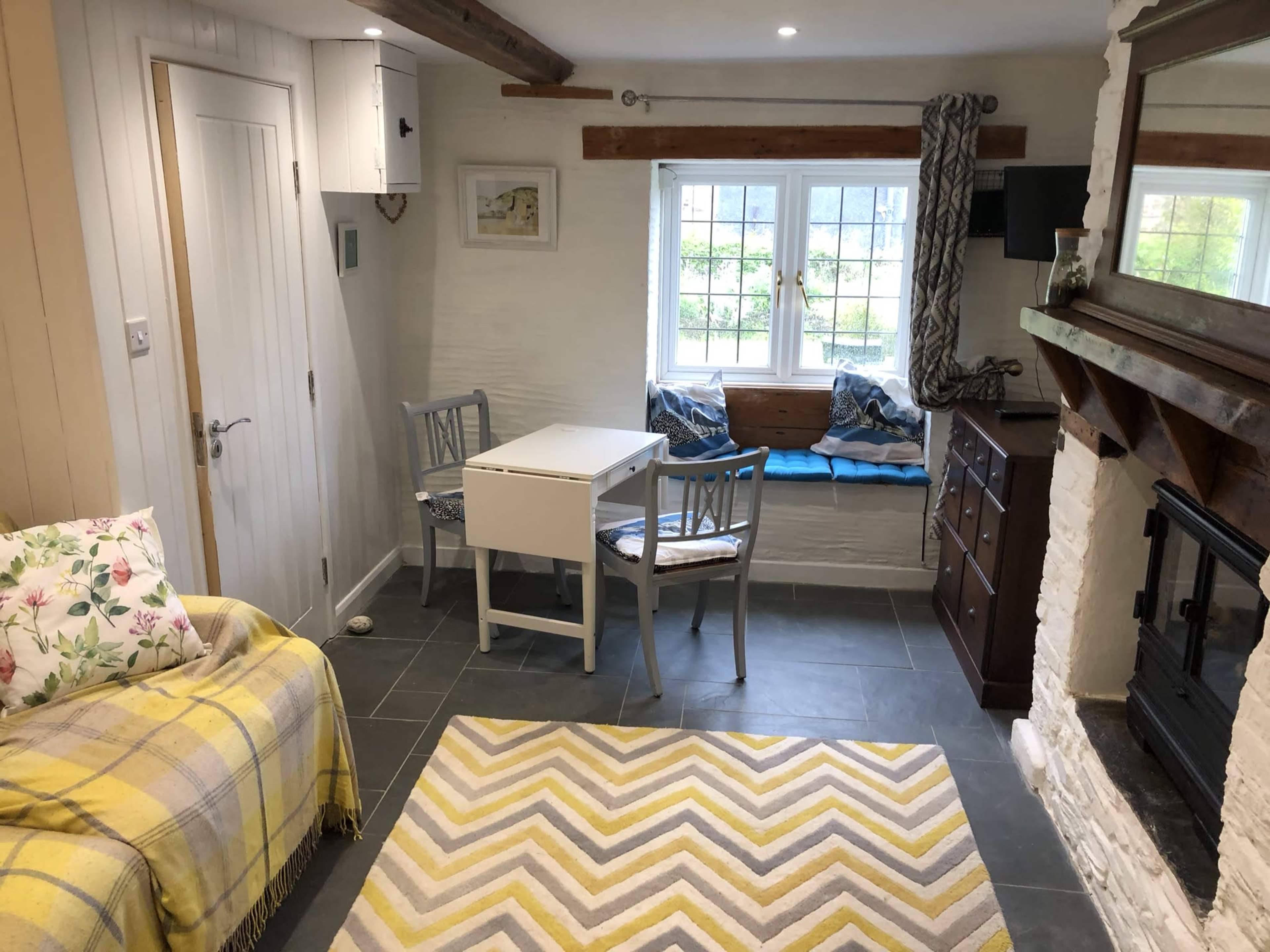 A cozy interior with a small dining table and chairs, a sofa with decorative pillows, a fireplace, and a window seat.