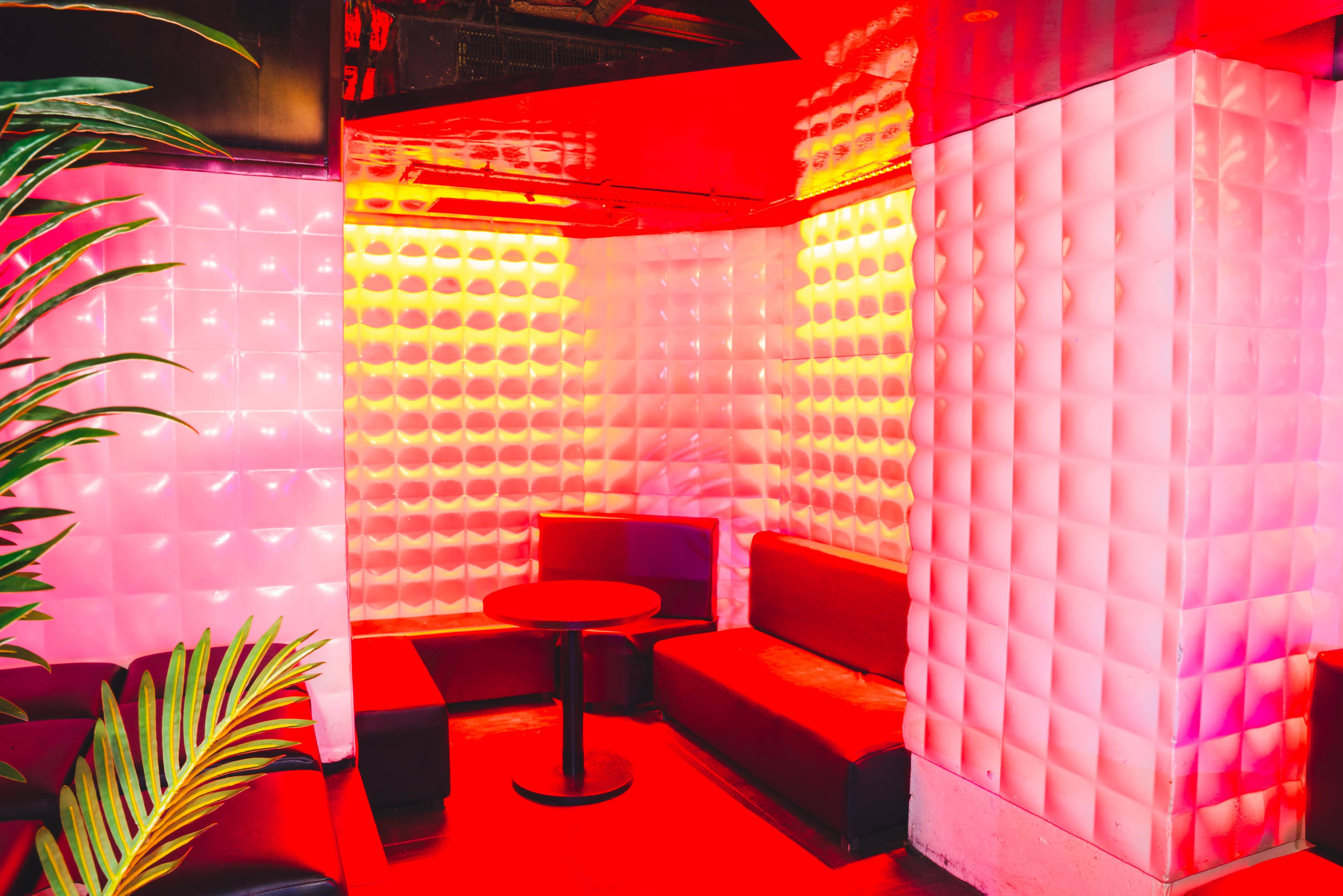 A vibrant lounge area features minimalist seating and illuminated, textured walls in shades of pink and red.