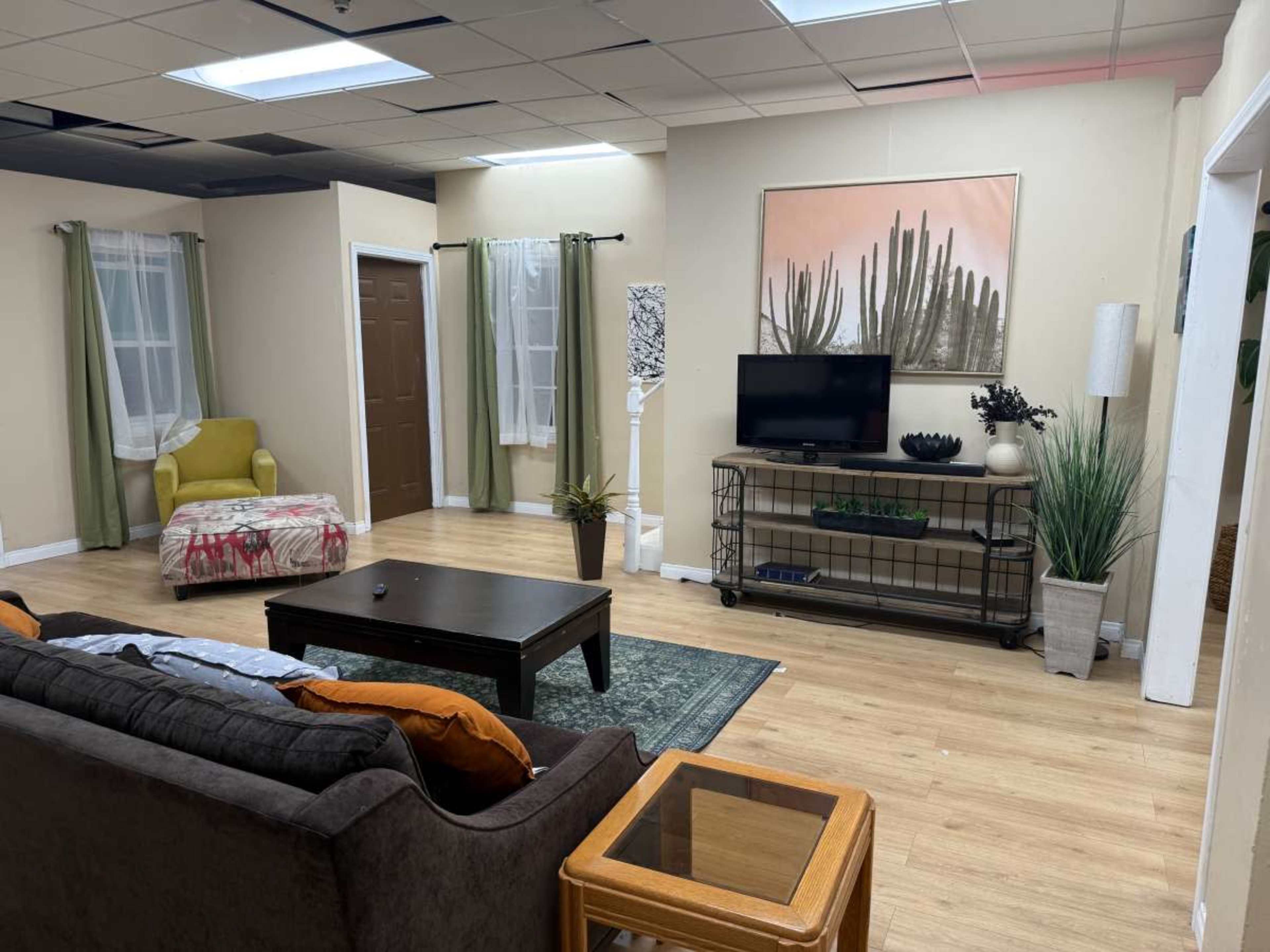 The image depicts a cozy living room with a sofa, a coffee table, a television on a stand, and various decorative plants and furniture.