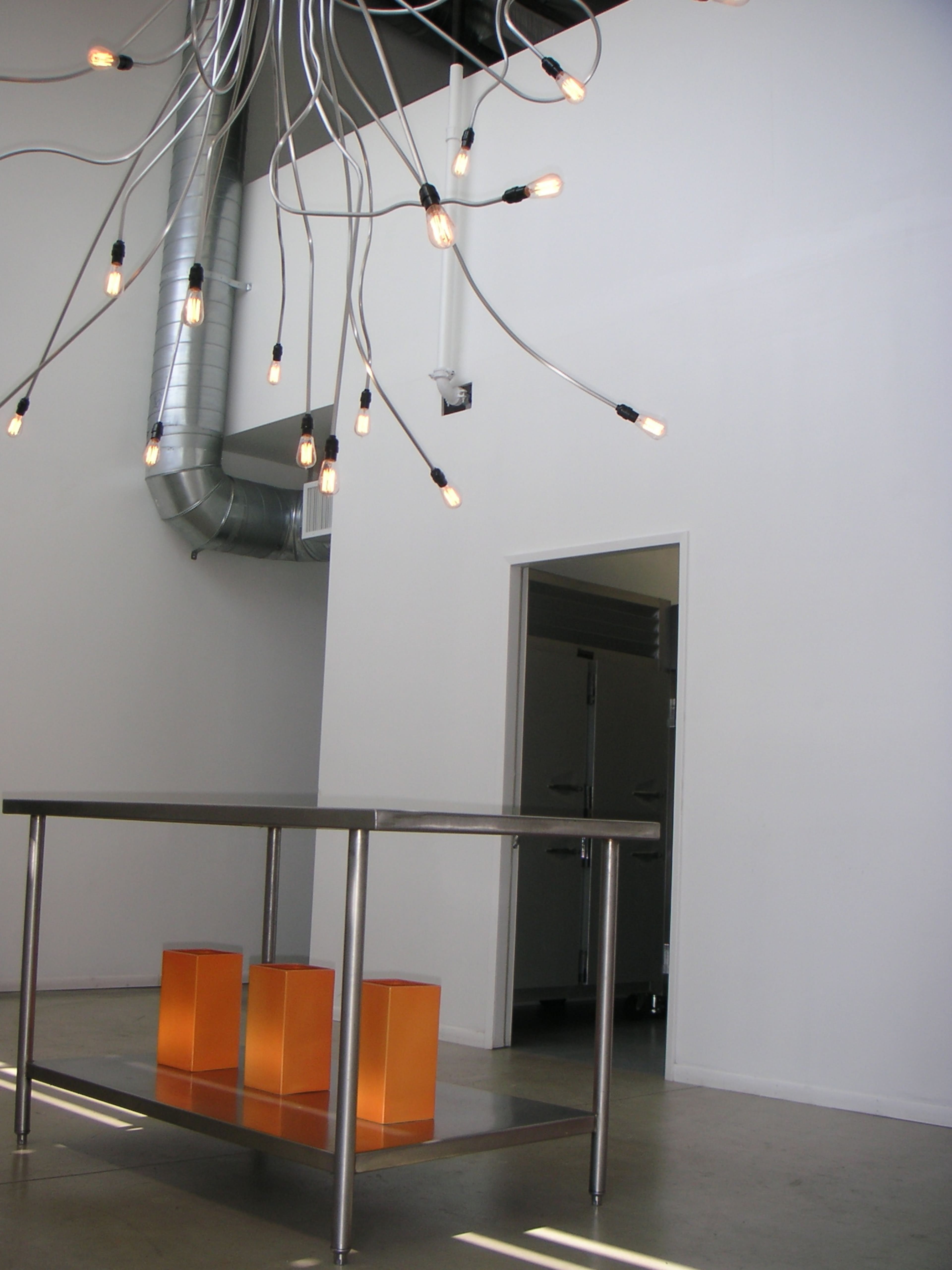 A modern, minimalist interior featuring a table with orange blocks as stools beneath a unique overhead light fixture.