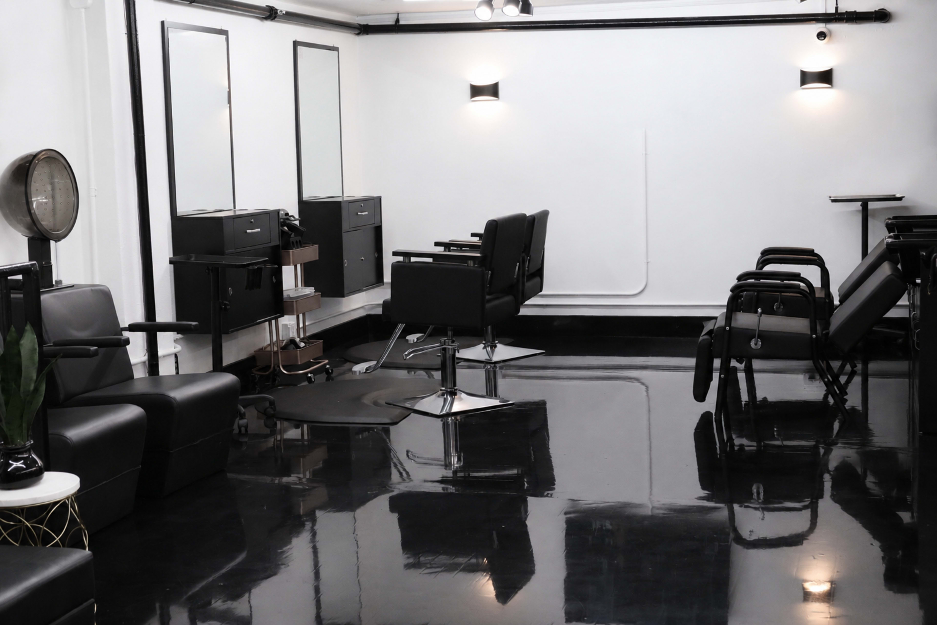 The image shows a modern hair salon featuring black chairs, mirrors, and a sleek, polished floor.