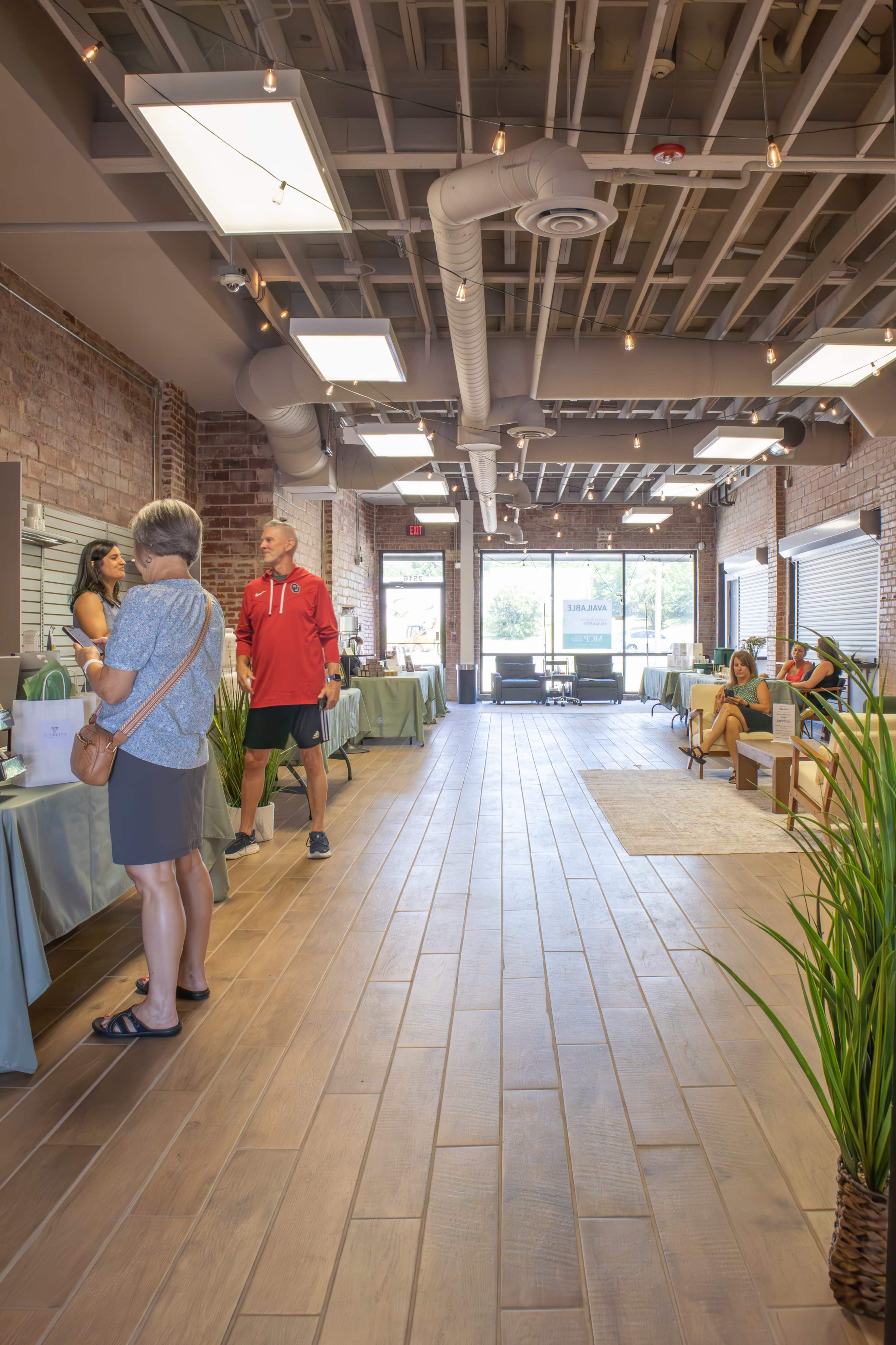 The image shows a modern, spacious interior of a wellness center with tables covered in green cloths and people engaged in conversations.