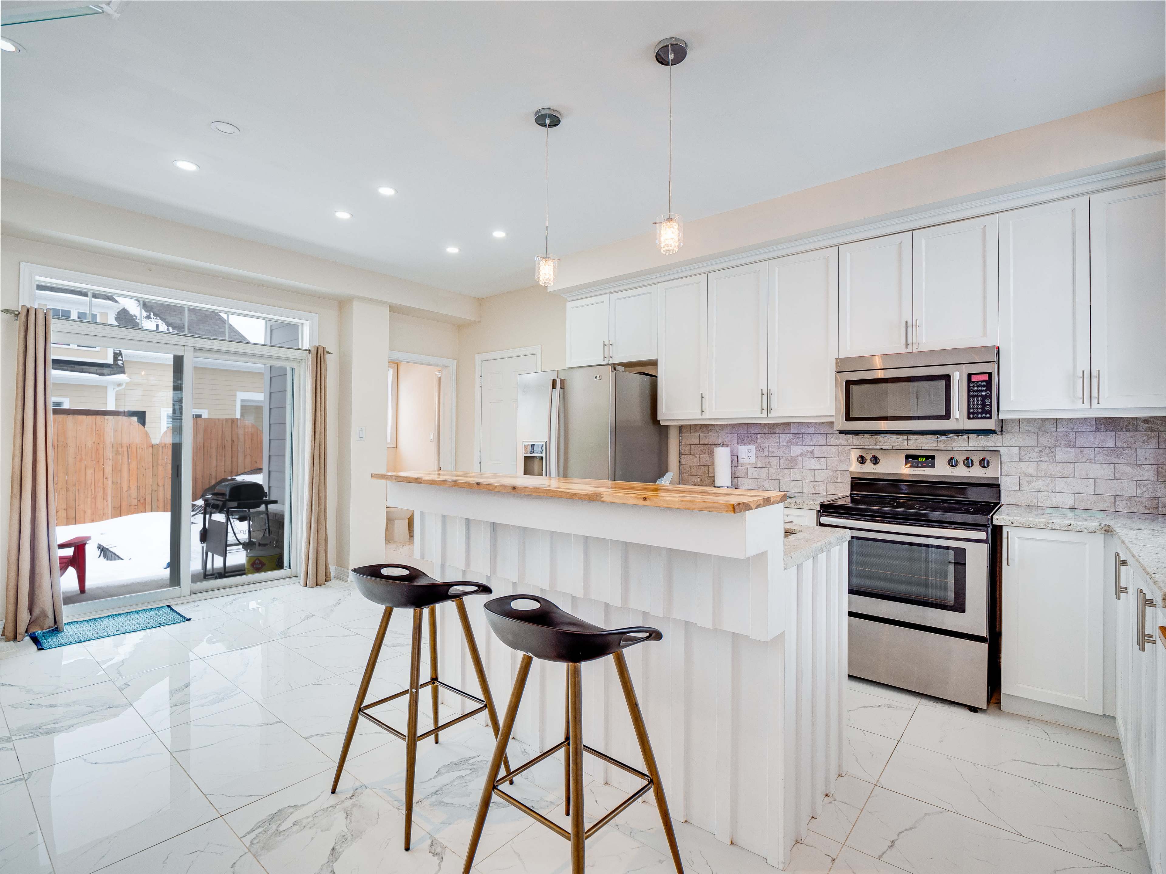 A modern kitchen features white cabinets, stainless steel appliances, and a central island with barstools, illuminated by pendant lights.