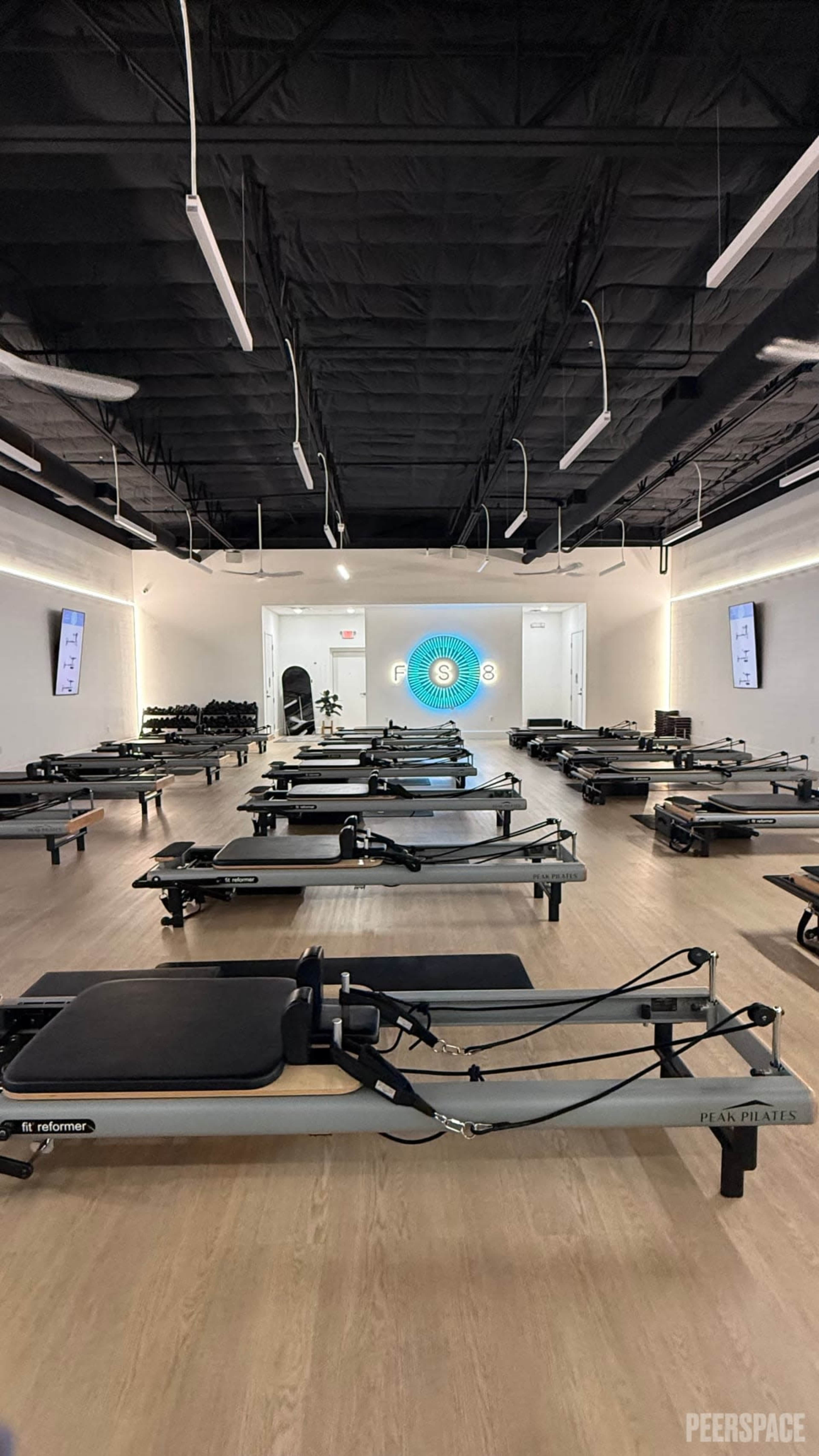 The image shows a spacious Pilates studio filled with multiple reformer machines arranged neatly in rows.
