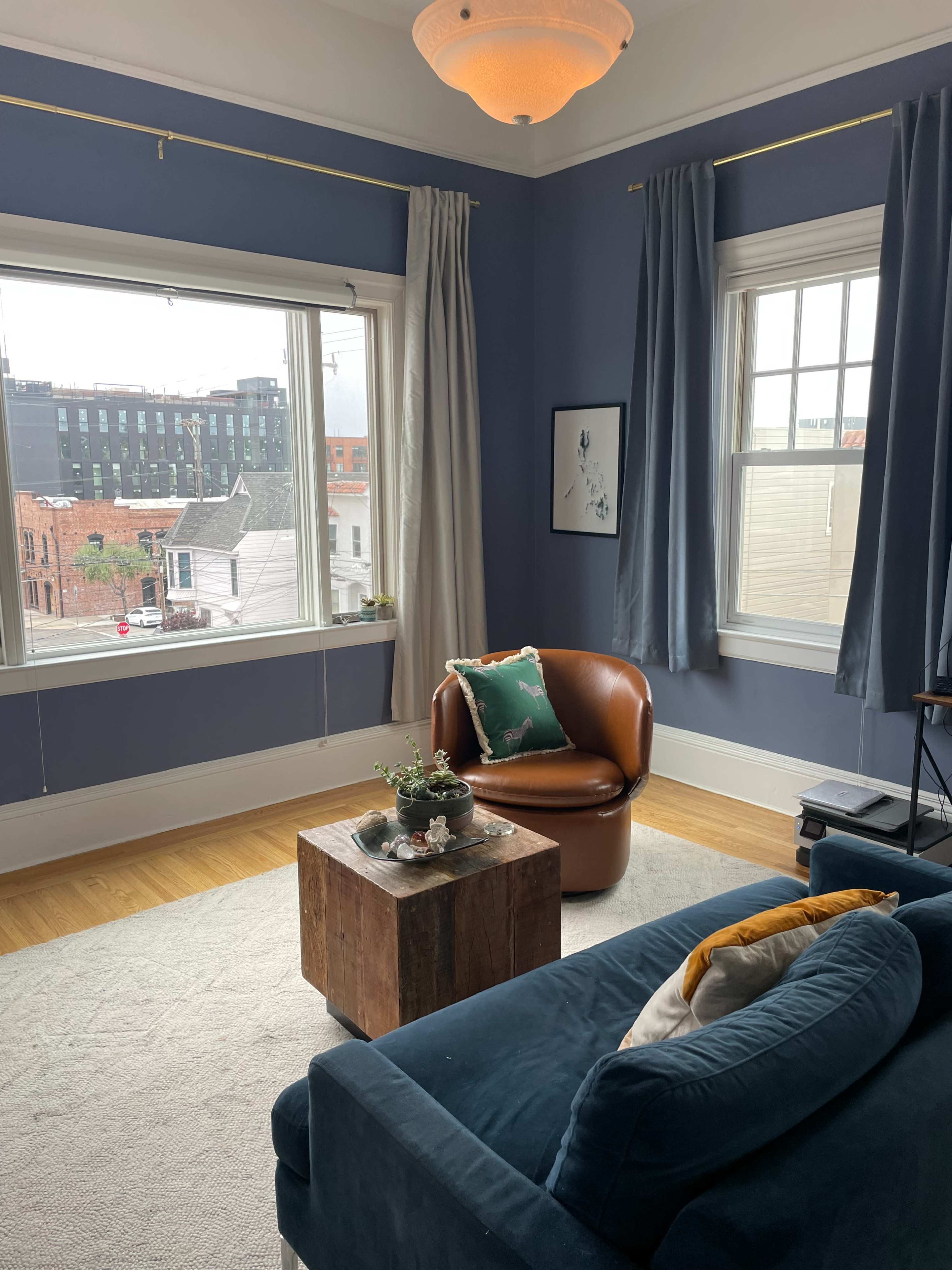 The room features a brown armchair, a wooden coffee table, and large windows with a view of a cityscape.