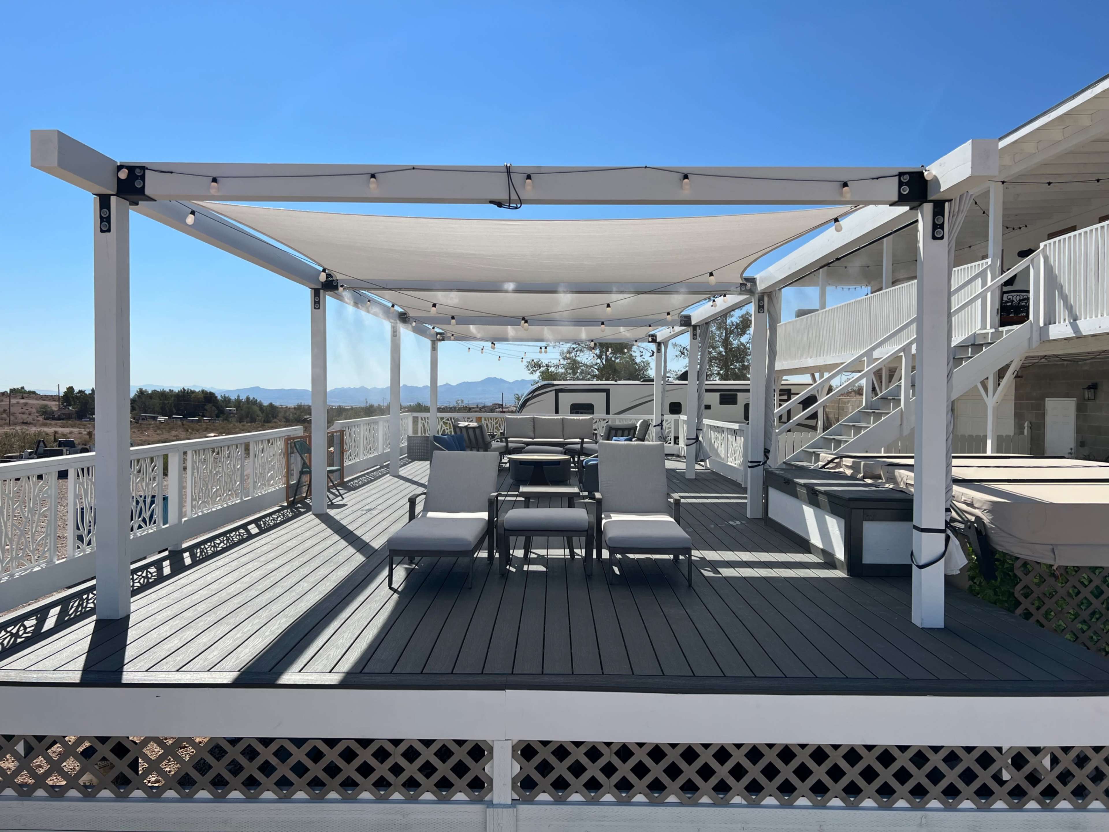 A spacious deck with a shaded seating area and a table, overlooking a landscape and mountains in the distance.