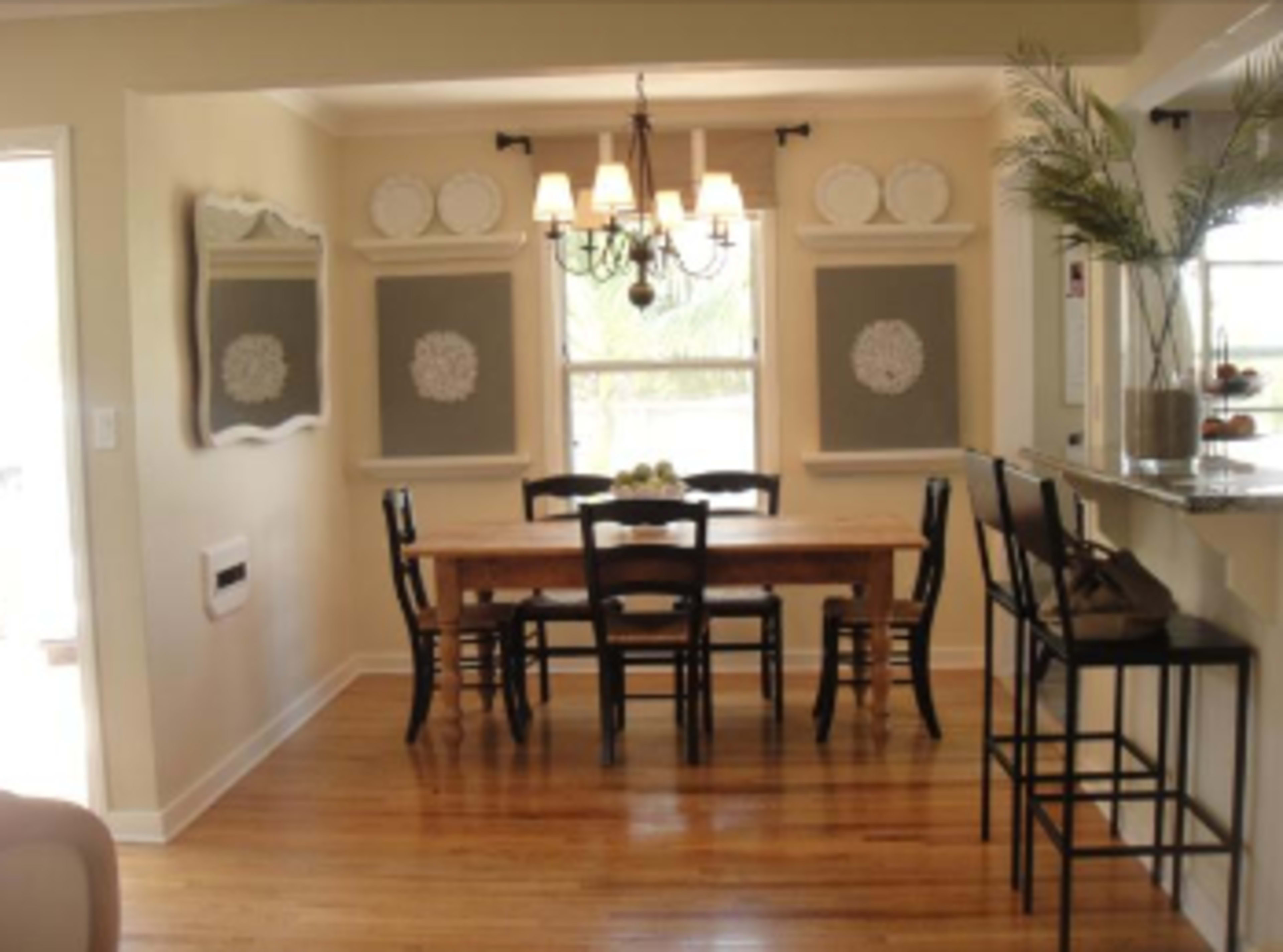 A dining area with a wooden table surrounded by black chairs, a chandelier overhead, and decorative elements on the walls.