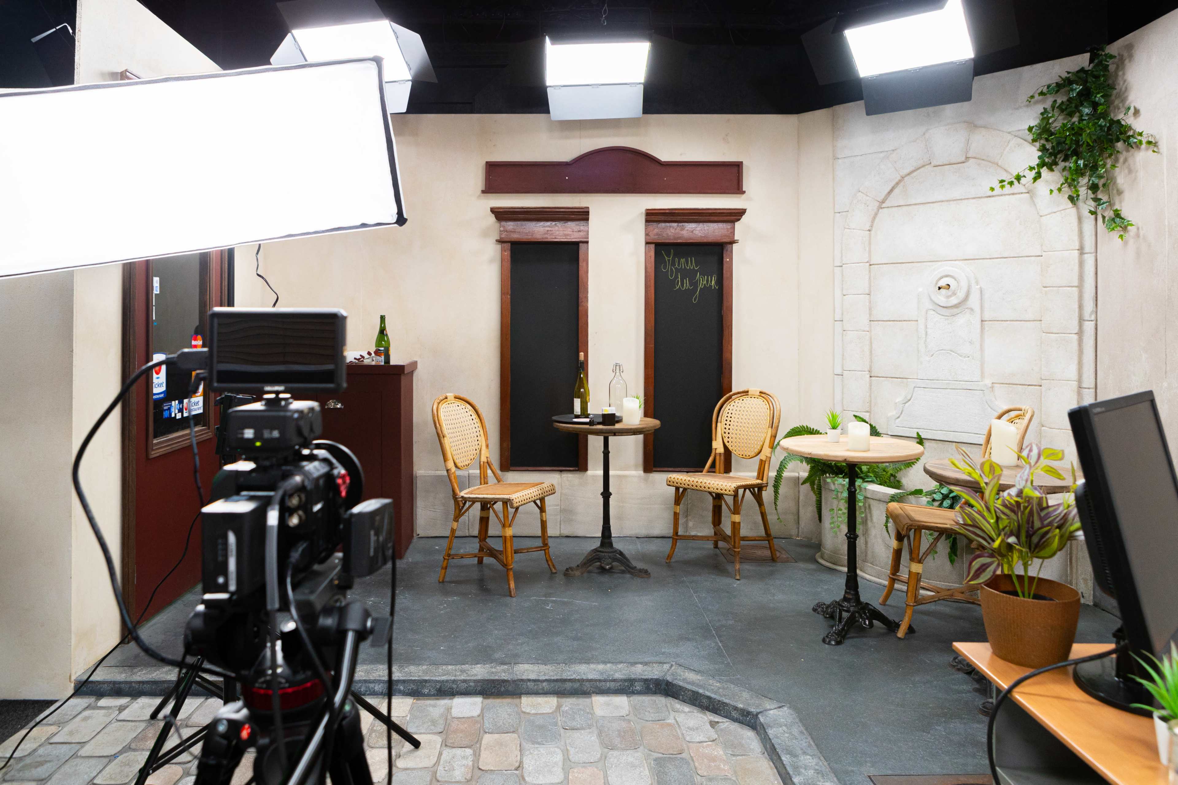 A small studio set with two bistro tables and chairs, a decorative wall fountain, and various lighting equipment.