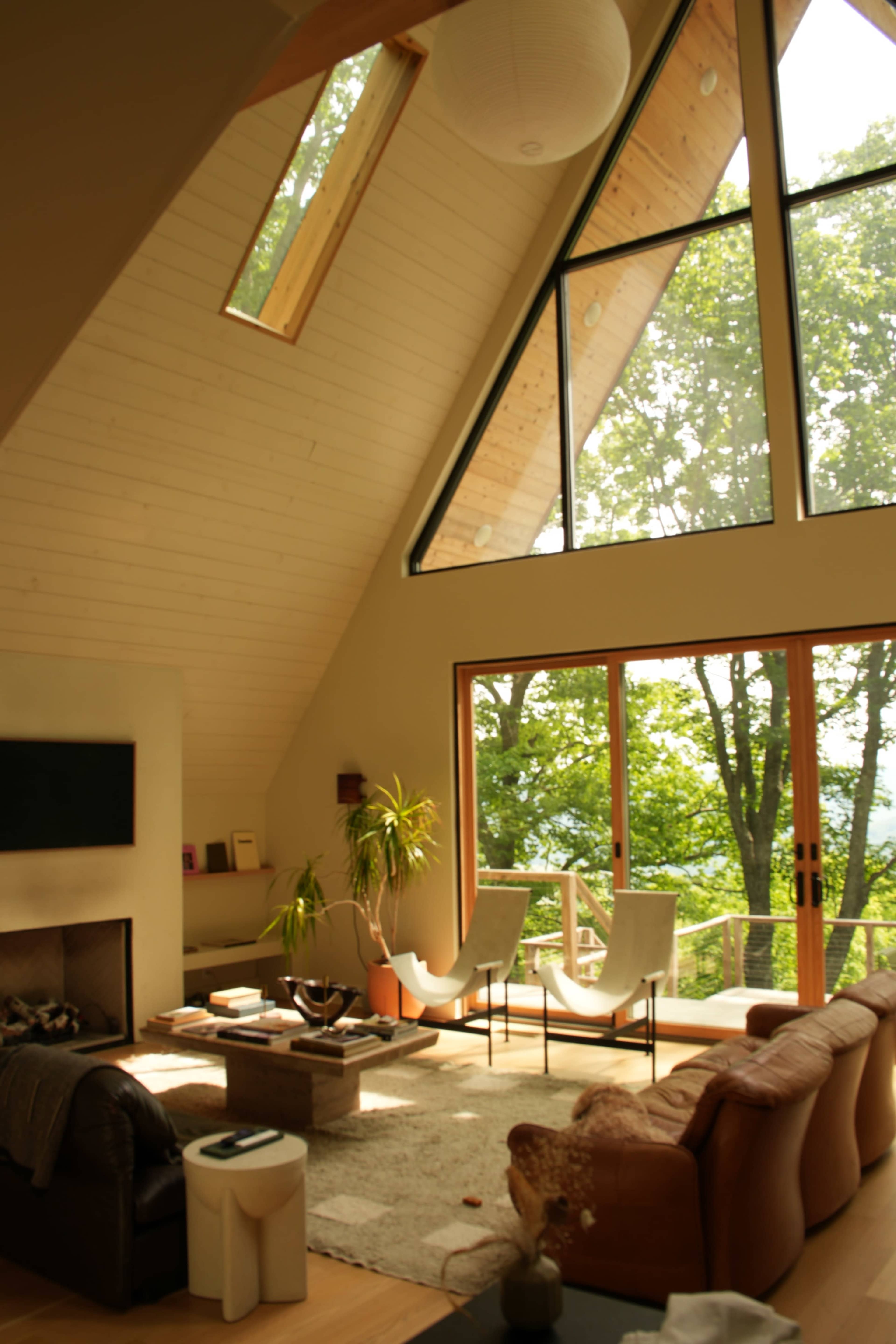 A spacious room features large triangular windows overlooking greenery, with modern furniture arranged around a central coffee table.