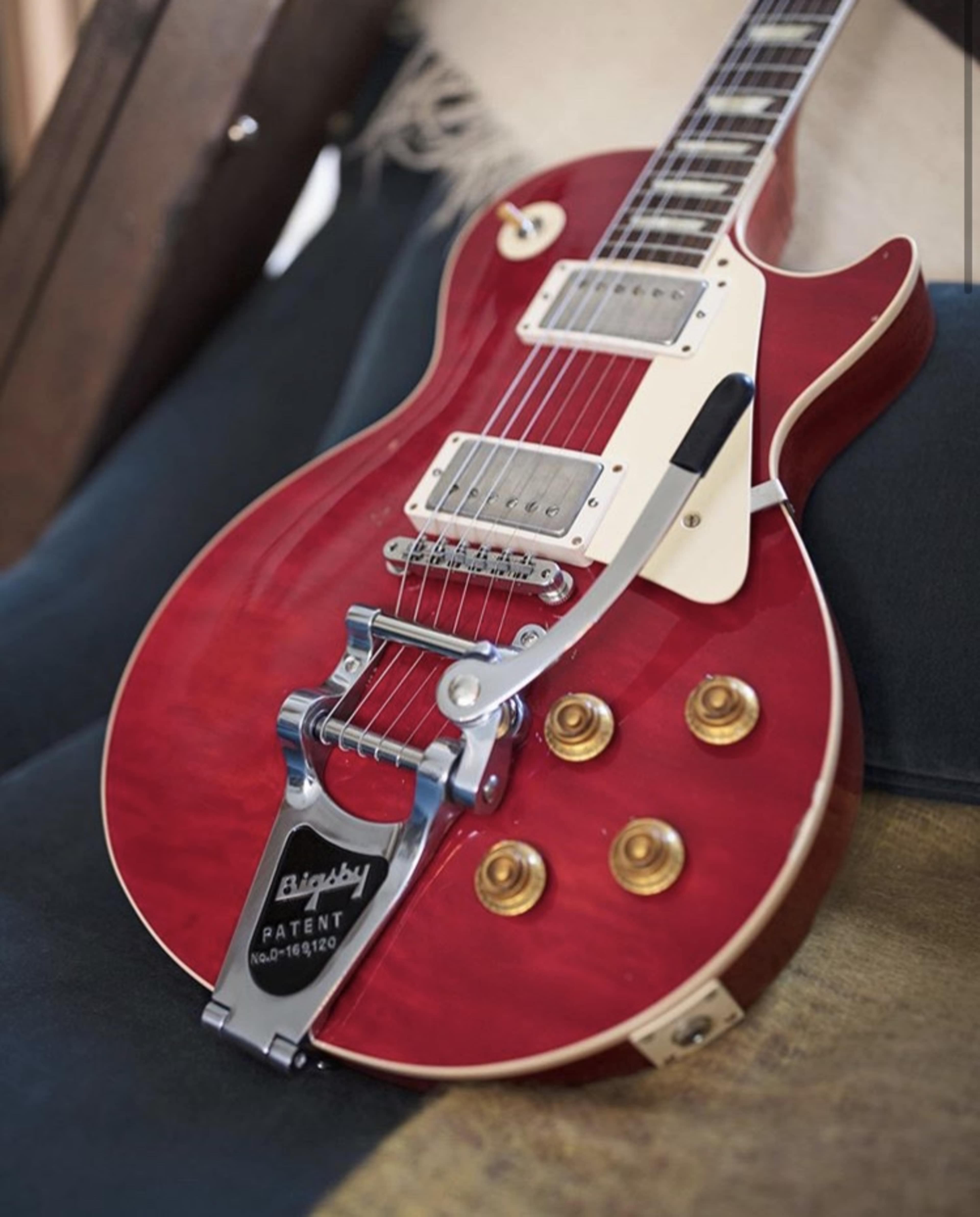 A red electric guitar with a Bigsby vibrato tailpiece rests on a textured surface.