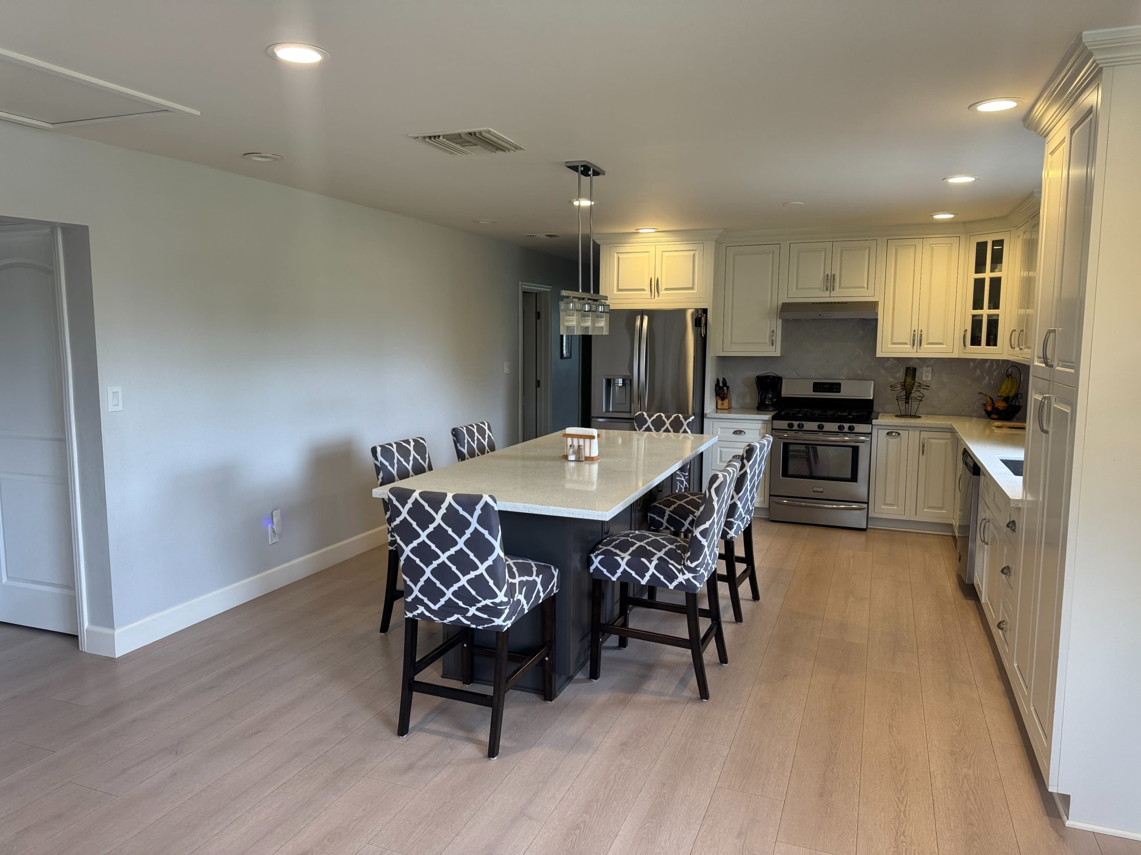 The image shows a modern kitchen featuring a large island with bar seating, light-colored cabinetry, and stainless steel appliances.
