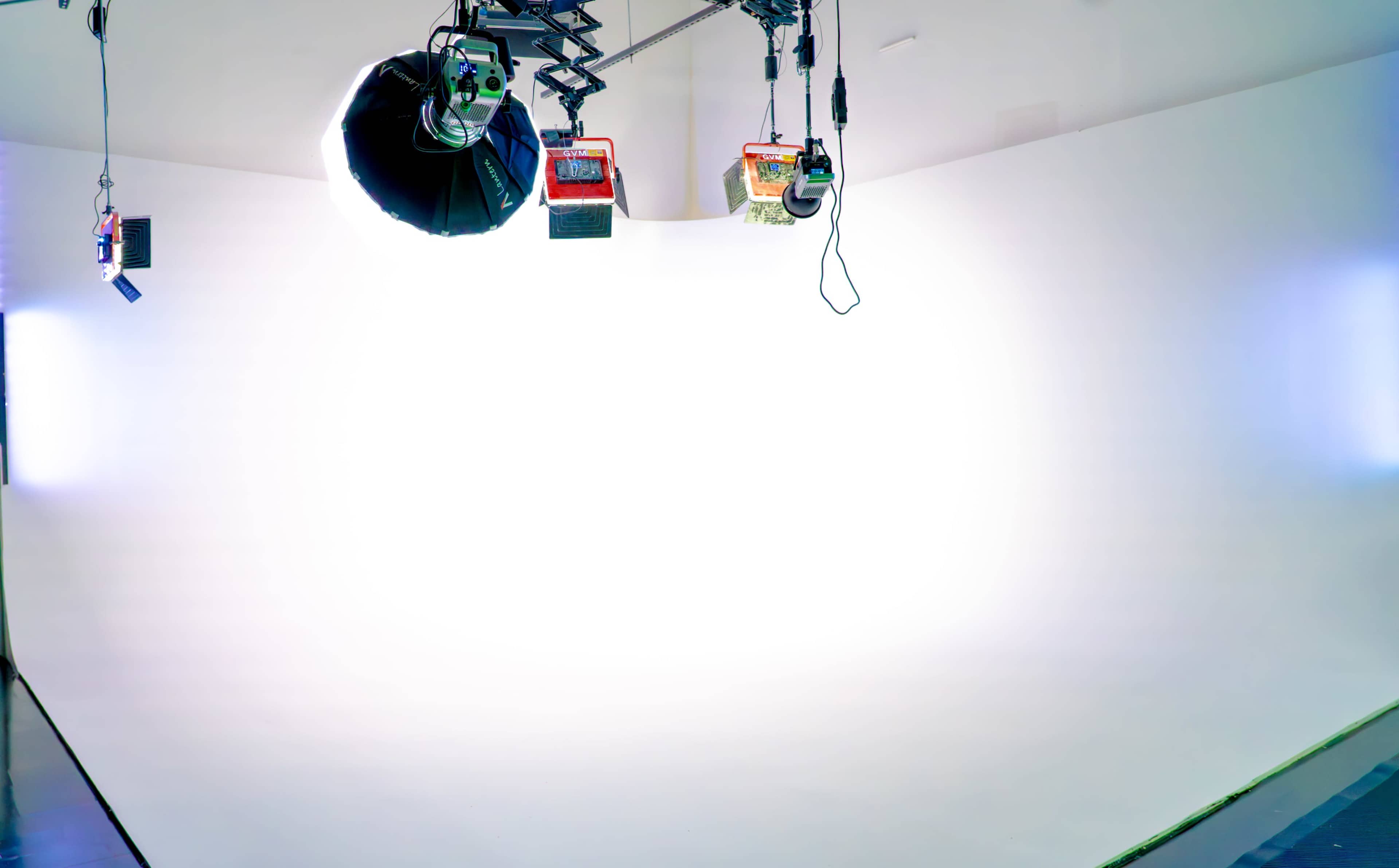 The image shows a photography studio with a bright white backdrop and multiple lights hanging from the ceiling.