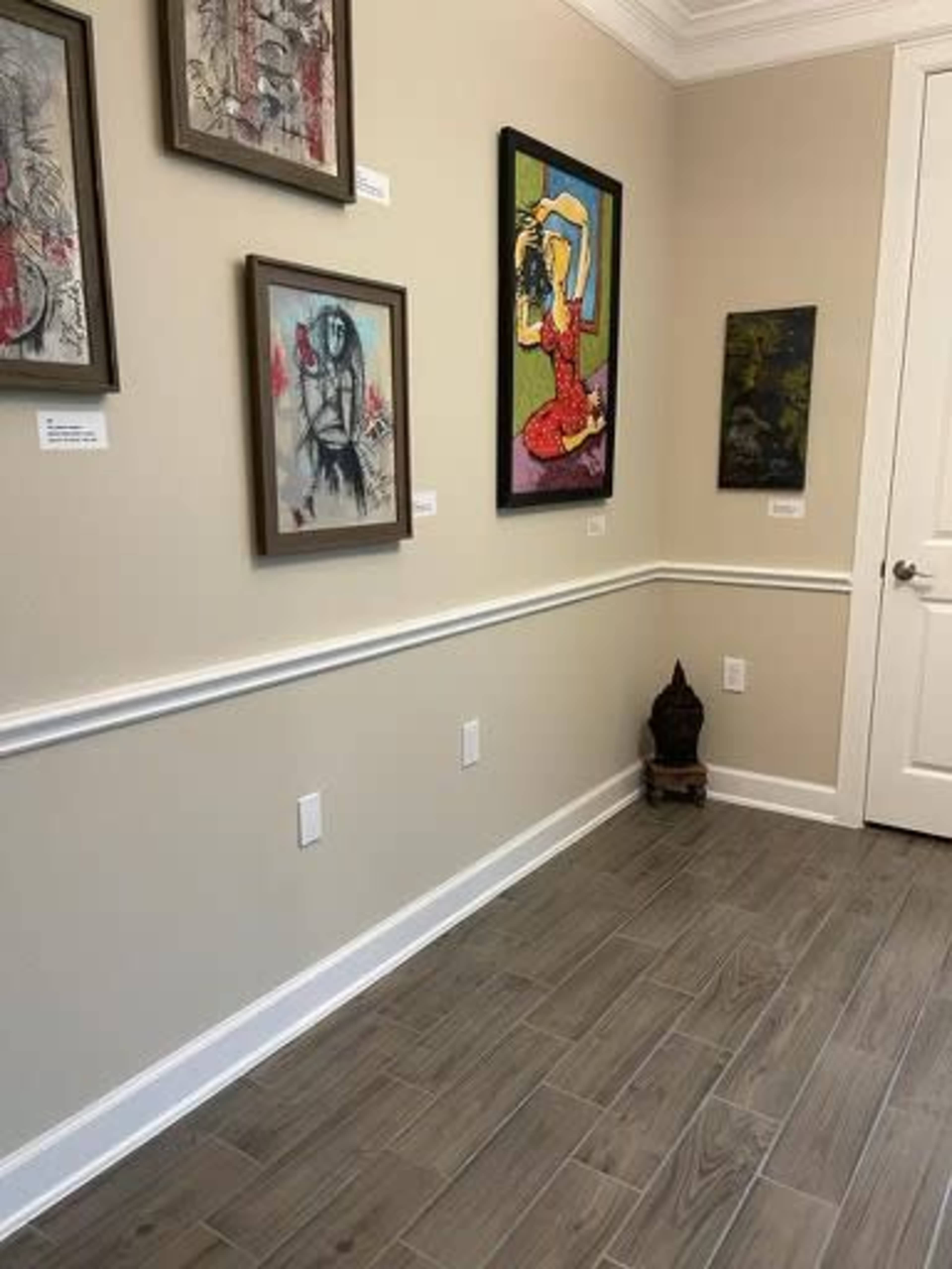 A gallery wall featuring various framed artworks and a small decorative statue in the corner, with tiled flooring and a doorway on the right.