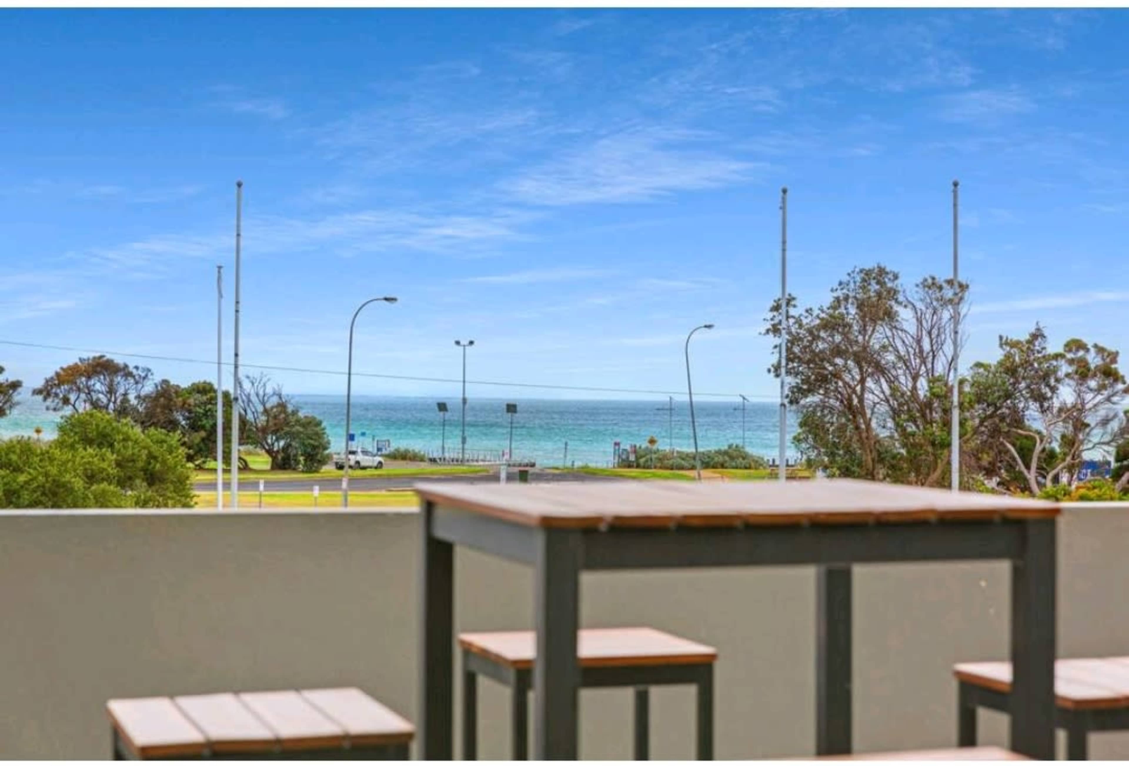 A view of the ocean from a balcony with wooden tables in the foreground.