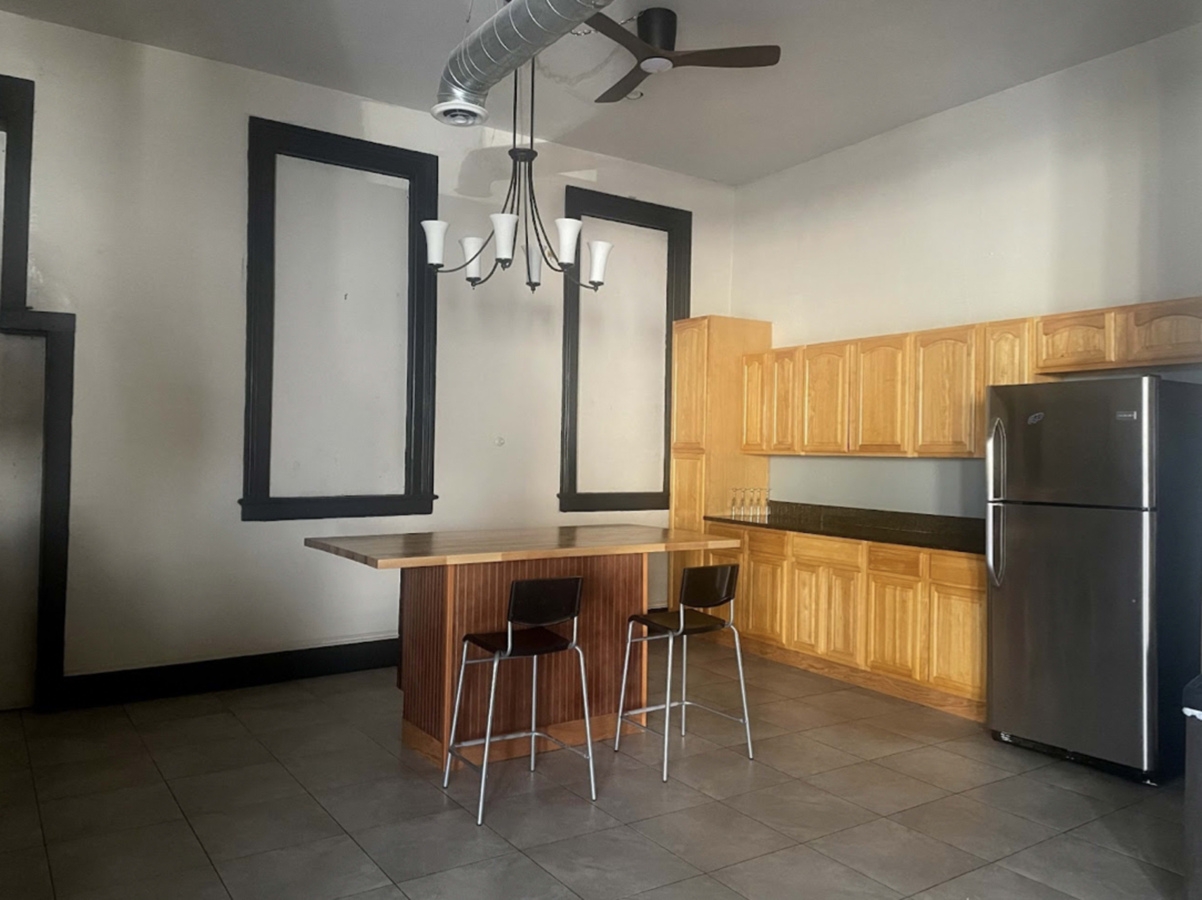 A spacious kitchen with a wooden island, two stools, a stainless steel refrigerator, and cabinetry against the wall.