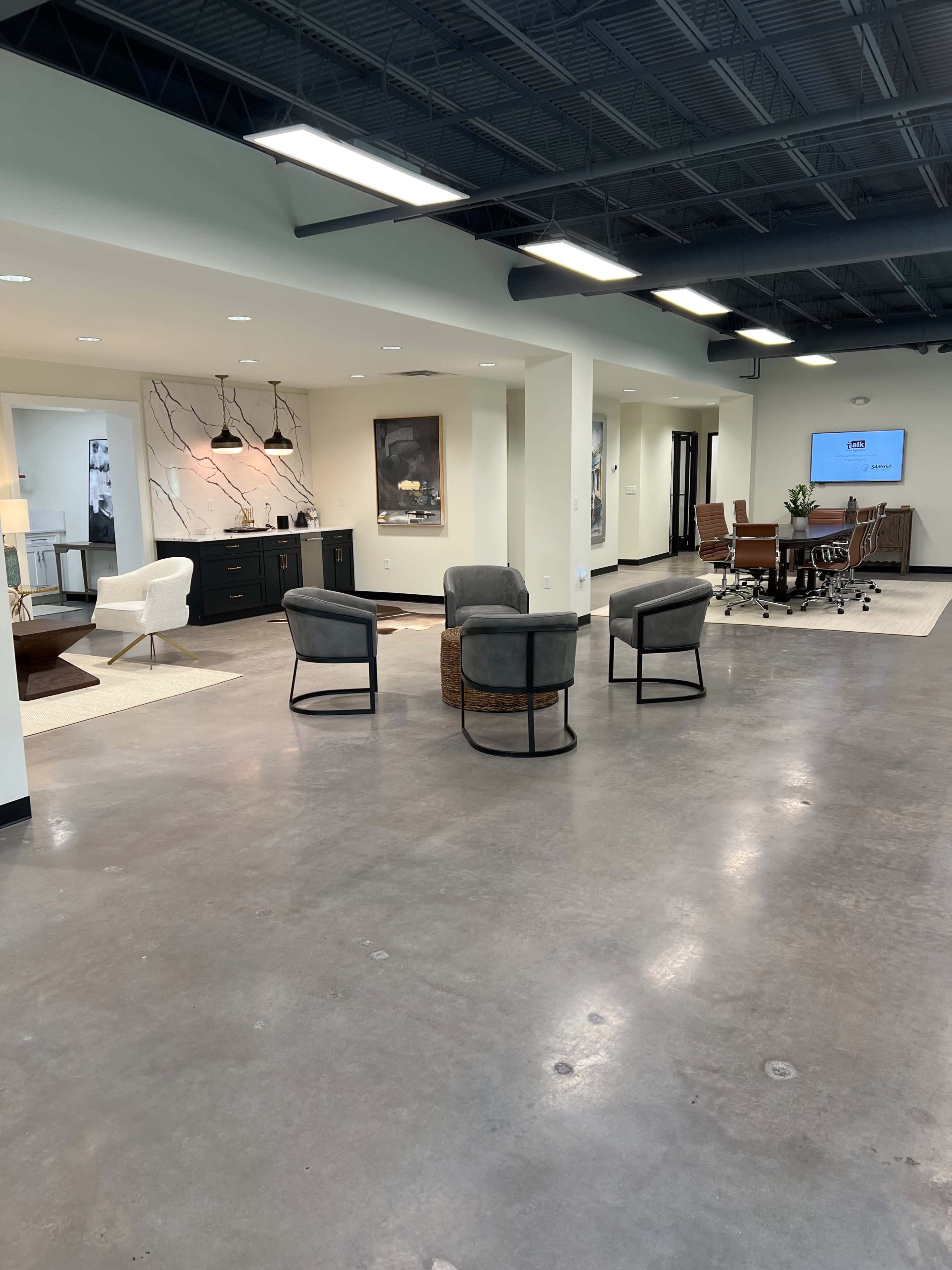 A spacious, modern office interior with a seating area, a kitchenette, and a meeting space equipped with a large table and chairs.