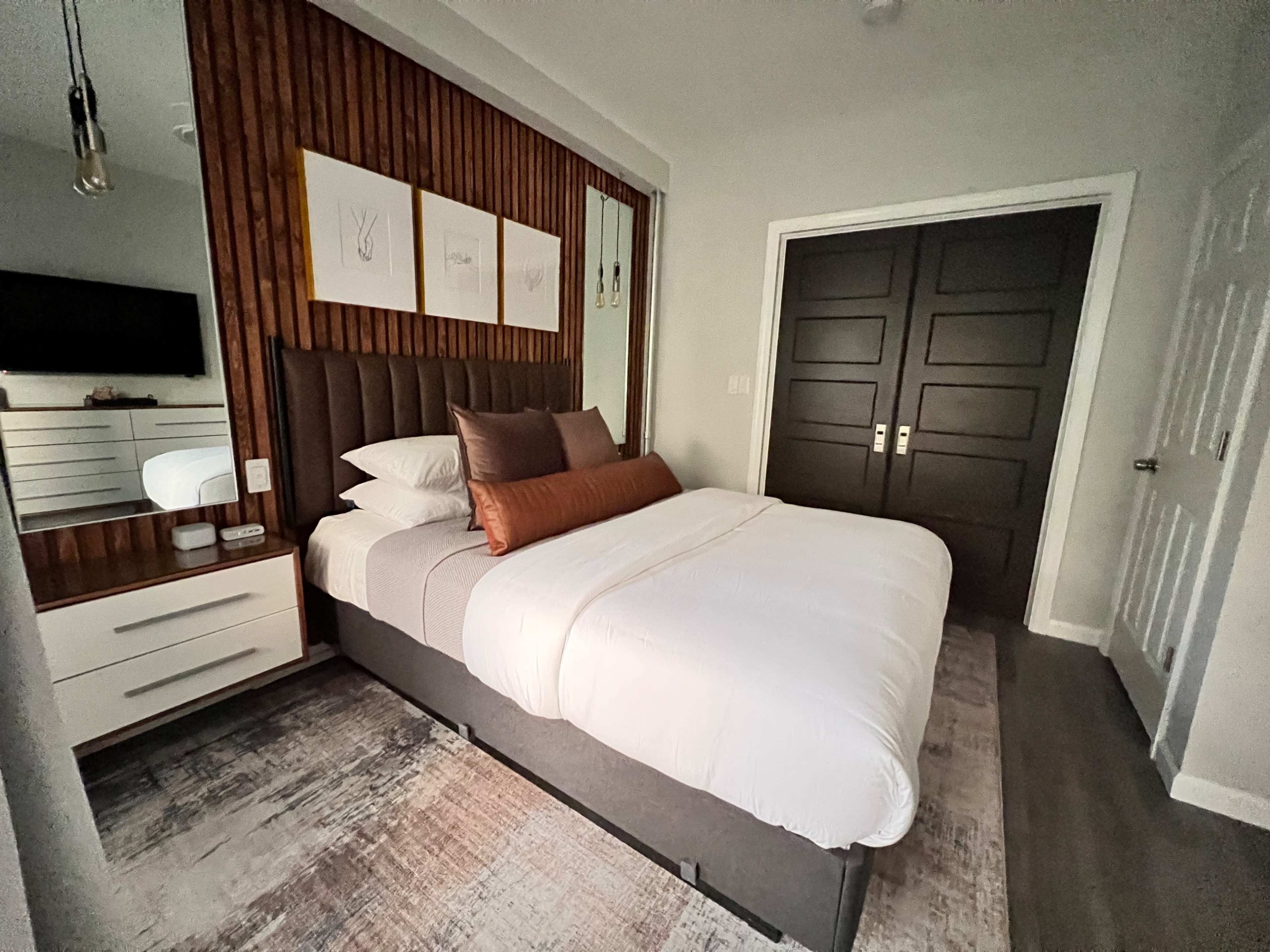 A modern bedroom with a queen-sized bed, dark wood accents, and a neutral color palette.