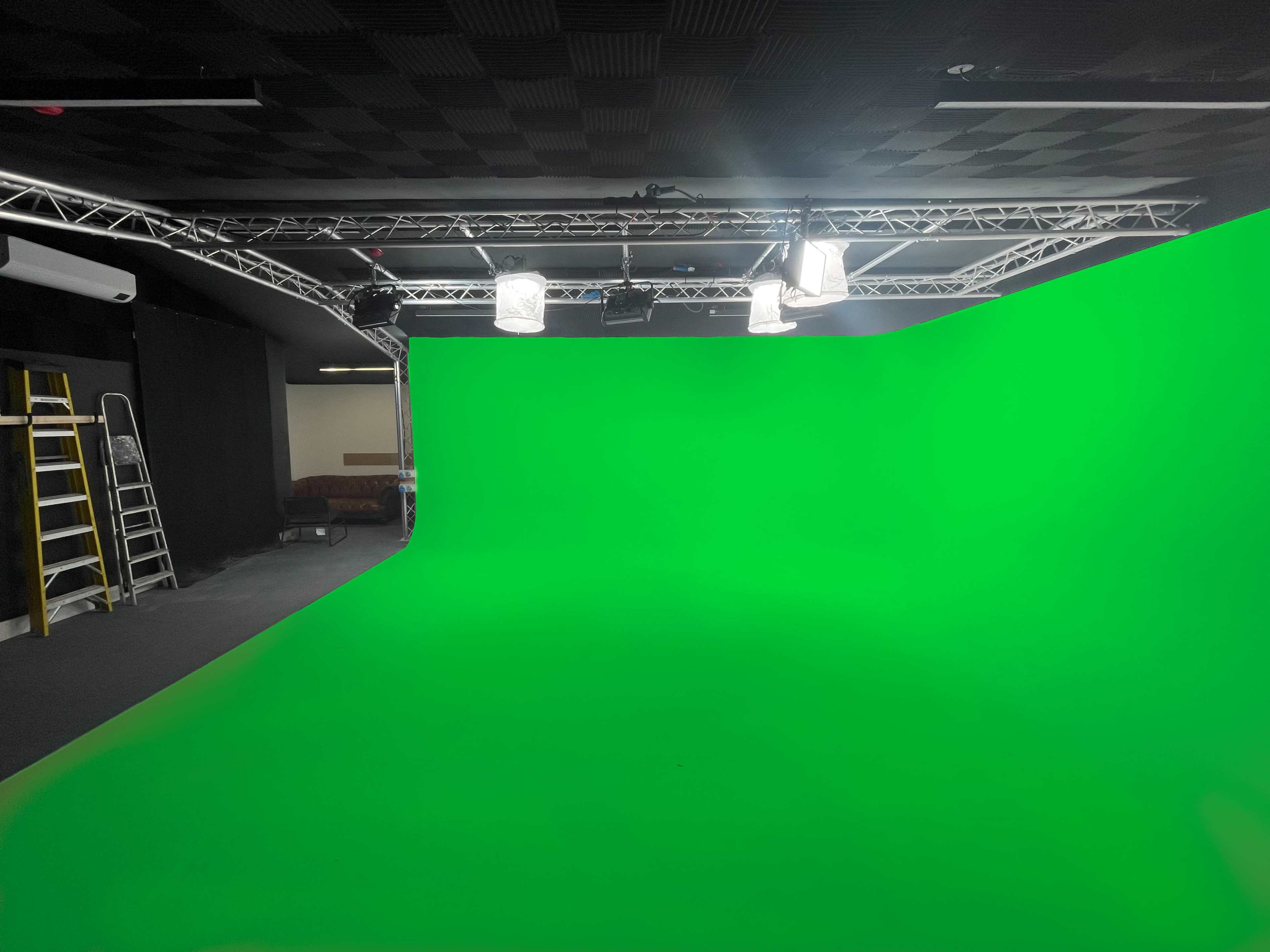 A green screen studio with lighting supports and a ladder against the wall.