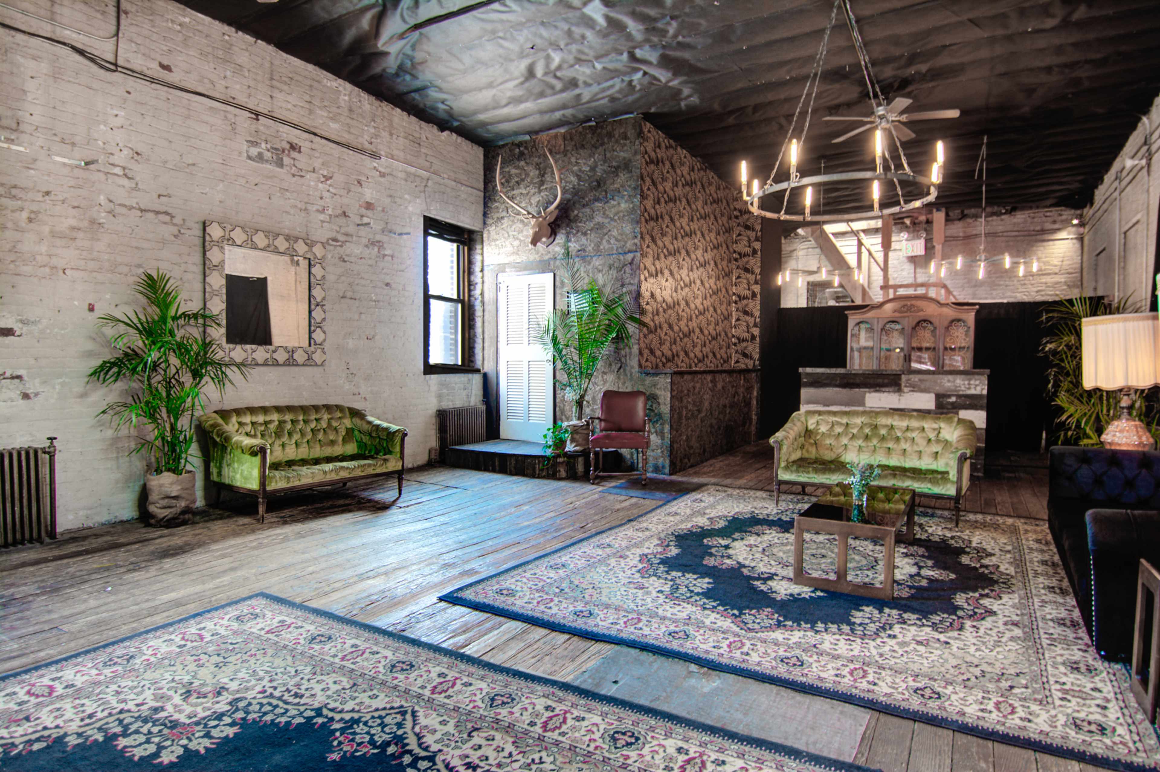 A spacious room with exposed brick walls, two green sofas, a large area rug, and a modern chandelier hanging from the ceiling.