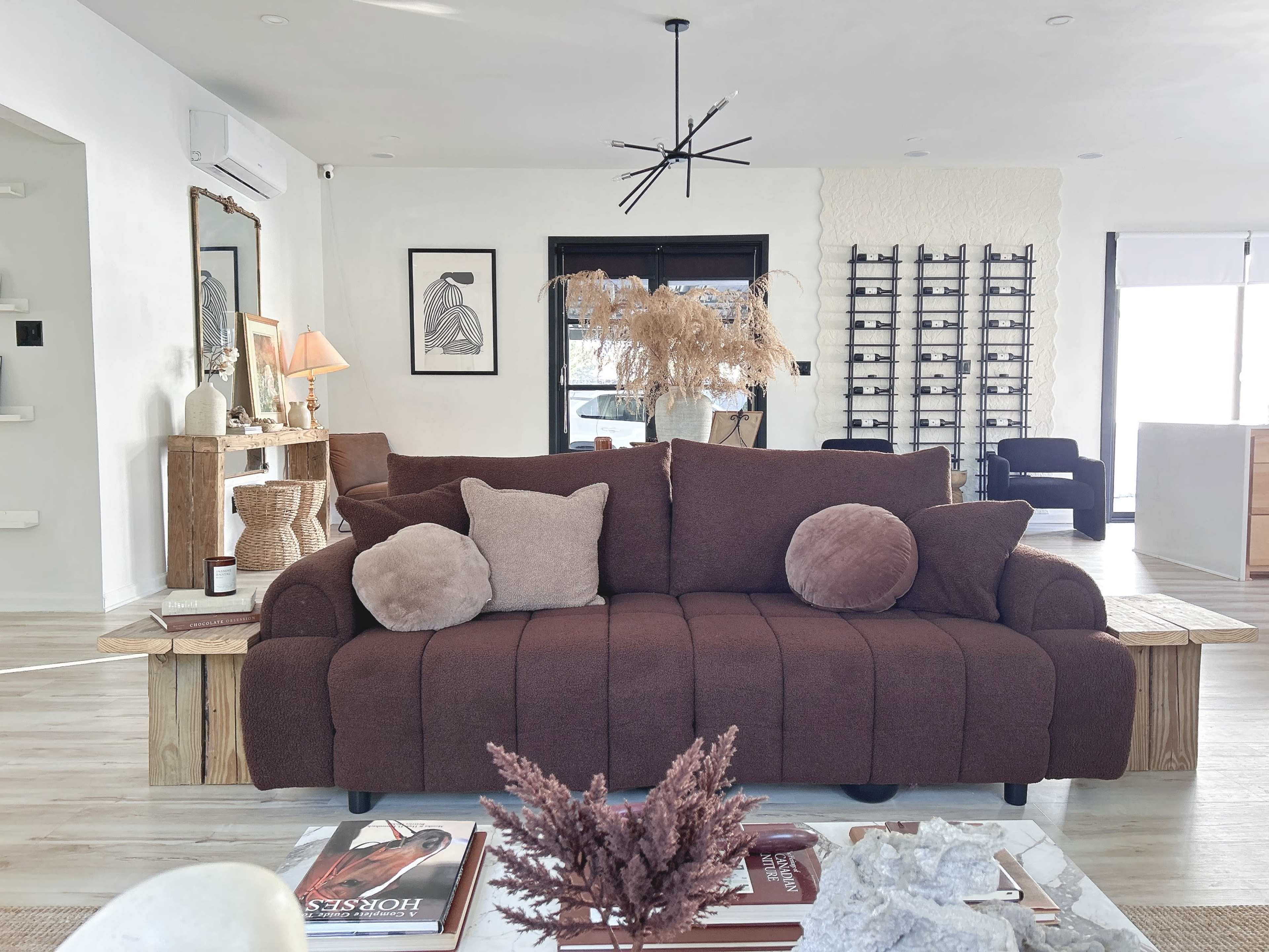 A brown sofa with assorted cushions sits in a modern living room adorned with decorative plants and artwork.
