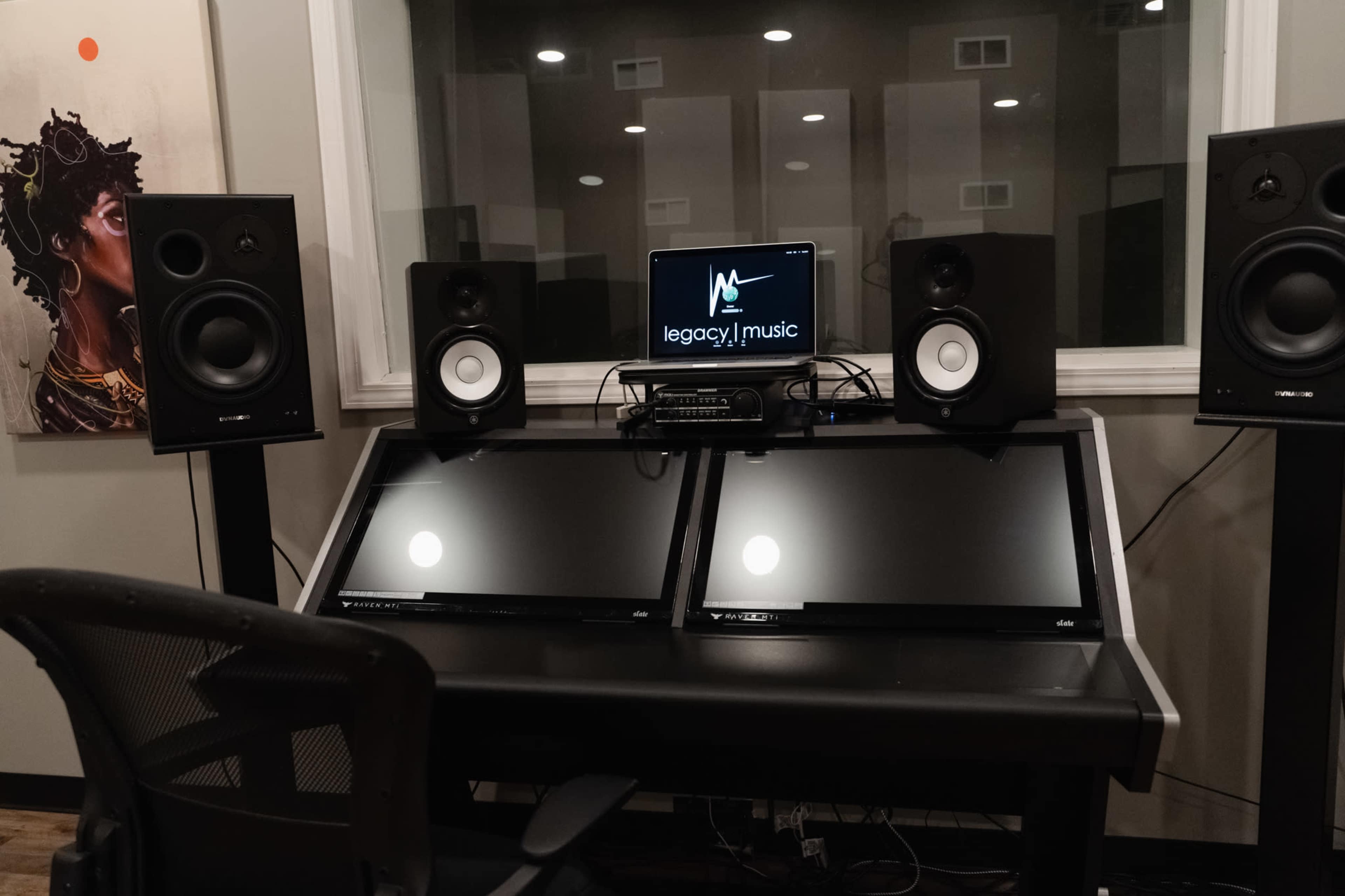 A music production studio featuring two computer monitors, studio speakers on either side, and a central mixing console with a logo displayed on the screen.