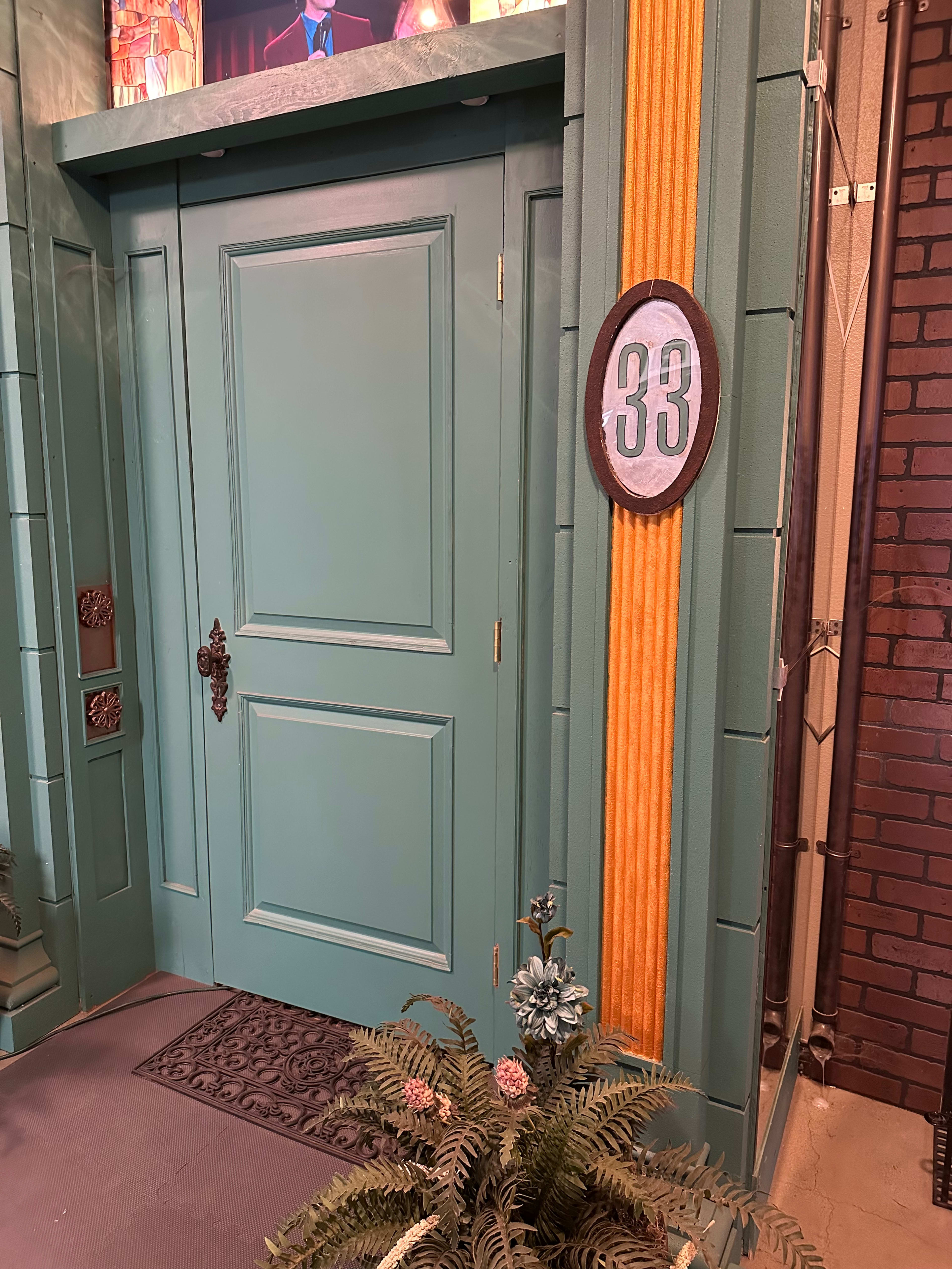 A teal door with the number 33 displayed on a round sign next to it, framed by vertical orange accents.