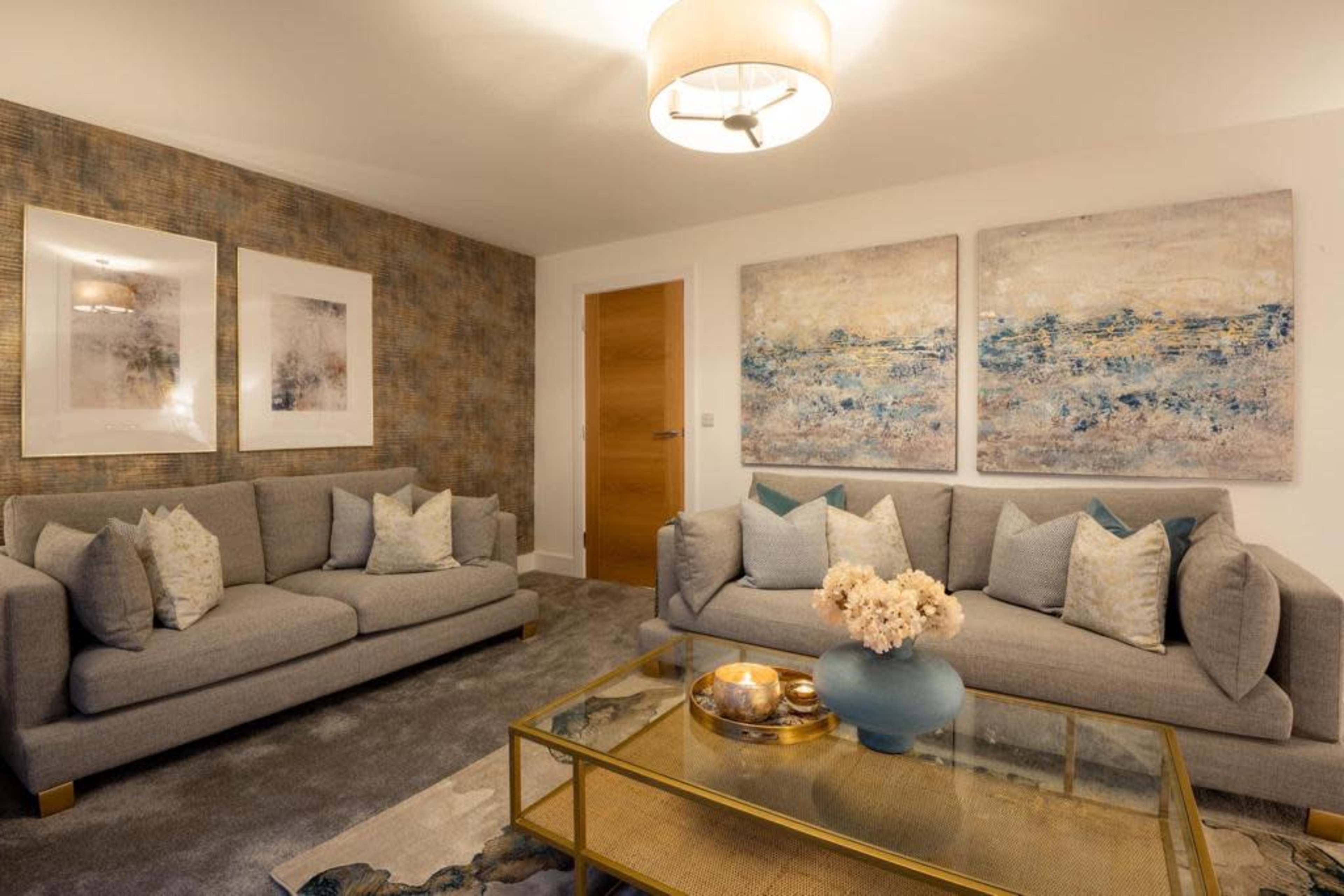 The image features a modern living room with two gray sofas, decorative pillows, artistic wall paintings, and a coffee table topped with a vase of flowers.