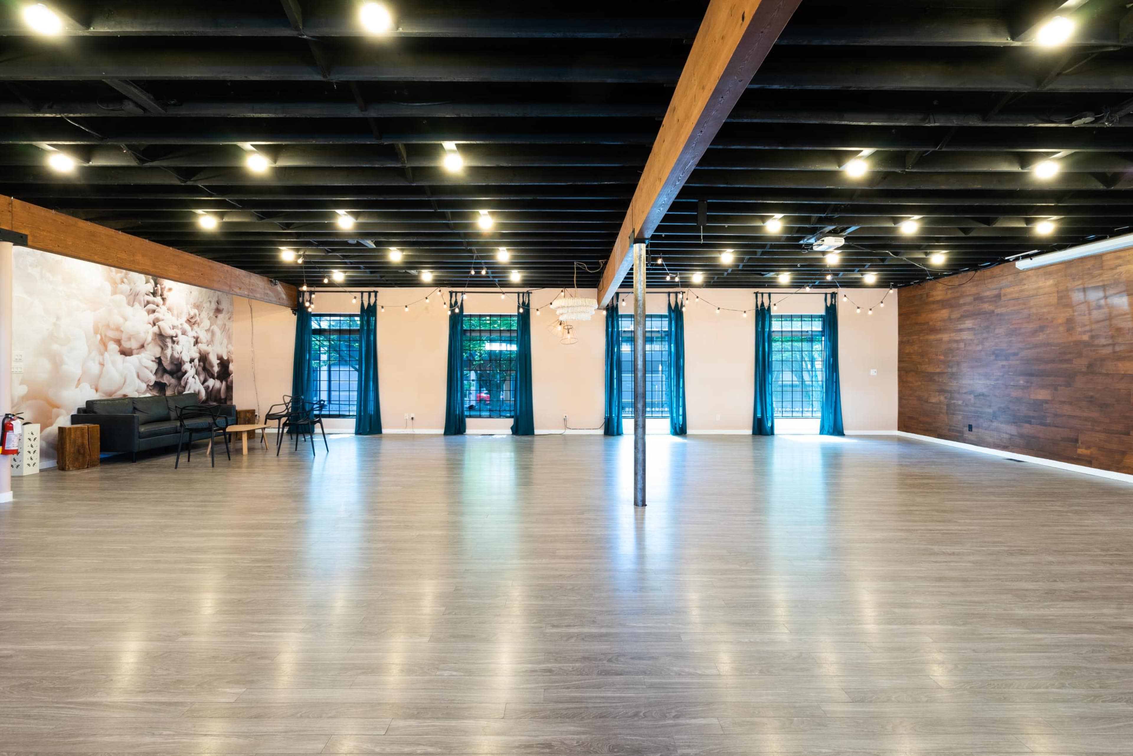 A spacious interior with wooden beams, polished gray flooring, and large windows, illuminated by overhead lights.