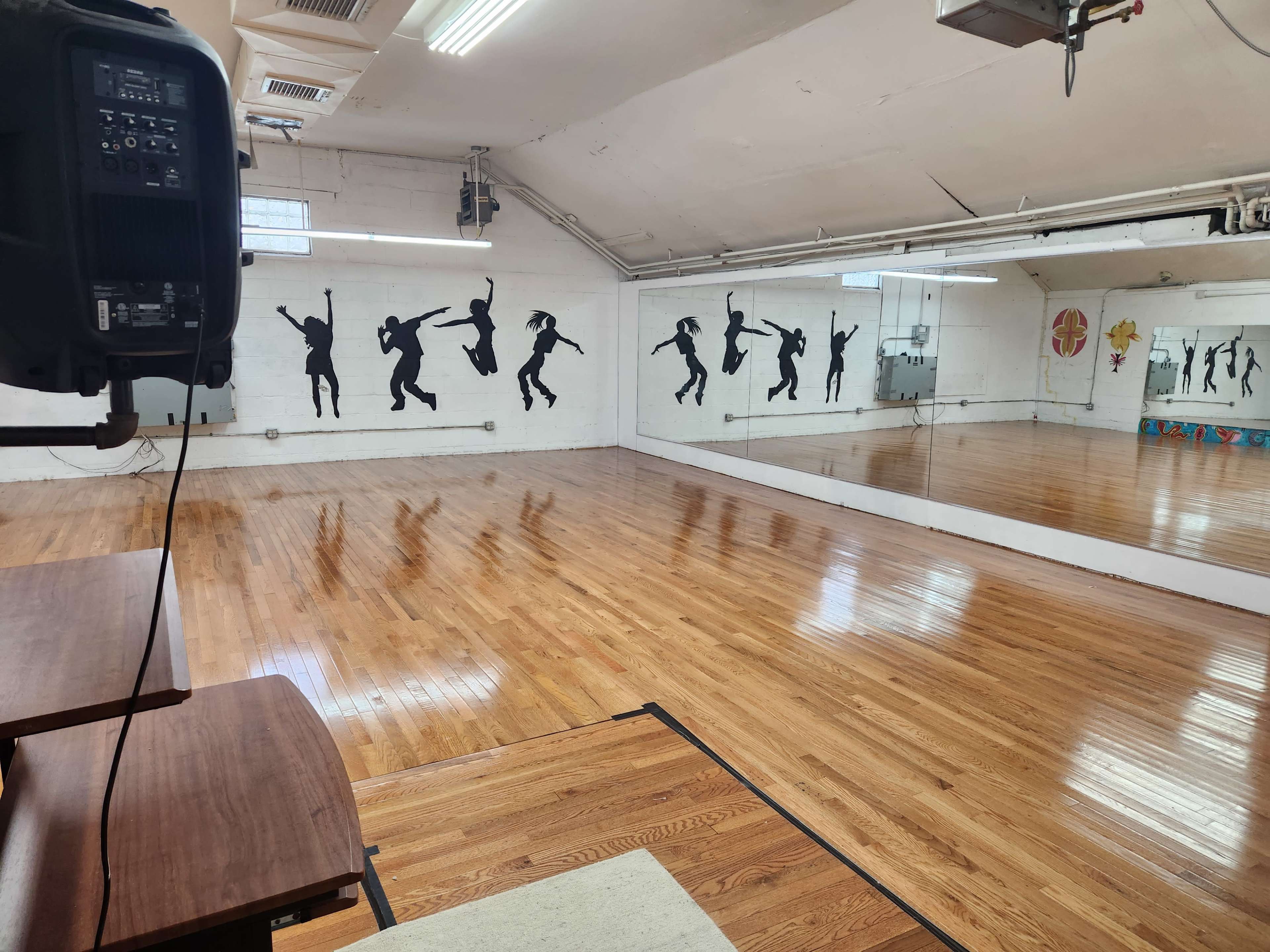 A spacious dance studio with wooden floors, mirrors on one wall, and silhouettes of dancers painted on another wall.