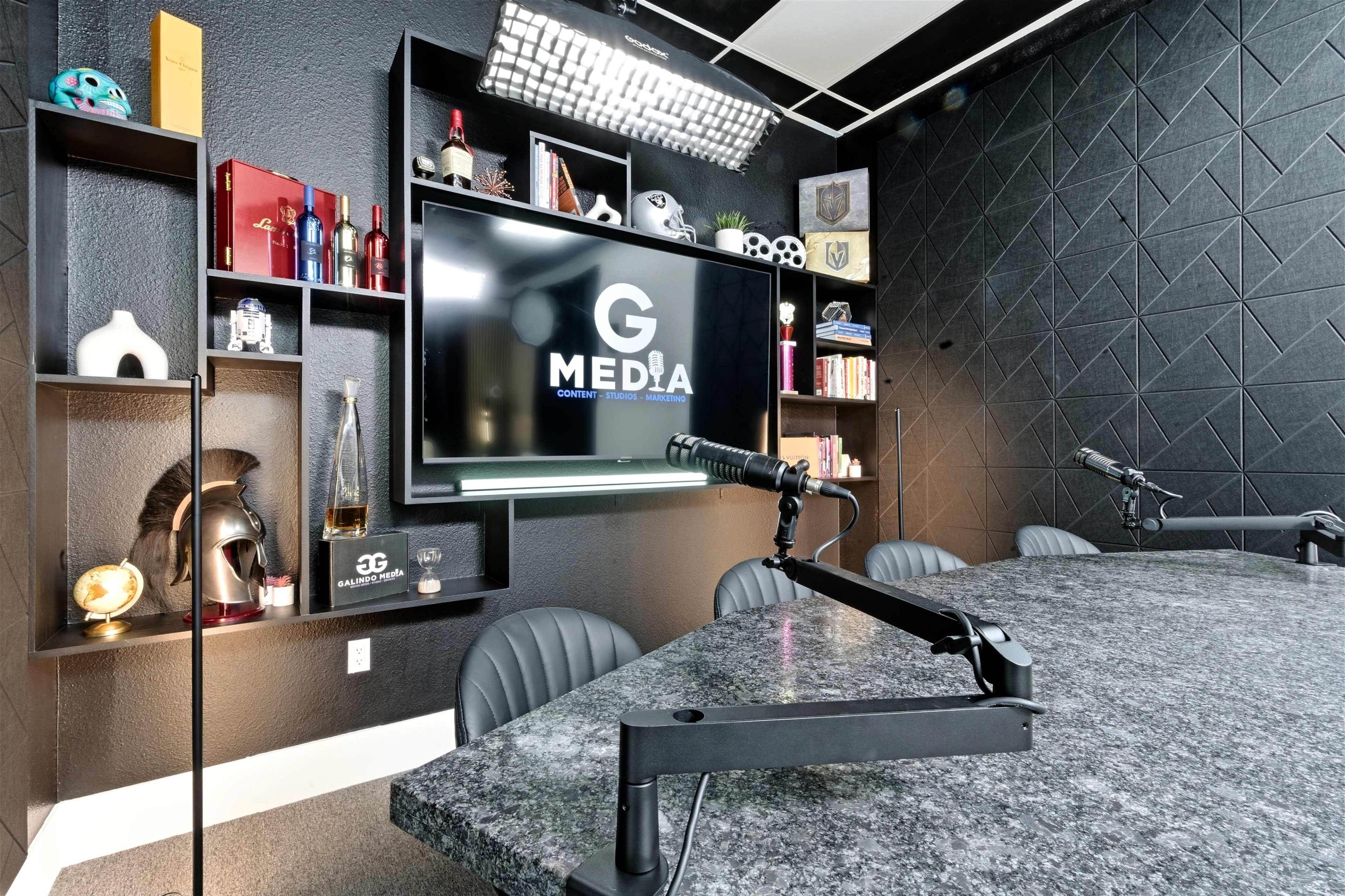 The image shows a modern conference room with a large screen displaying the logo "G MEDIA," surrounded by various decorative items and a granite table with microphone setups.