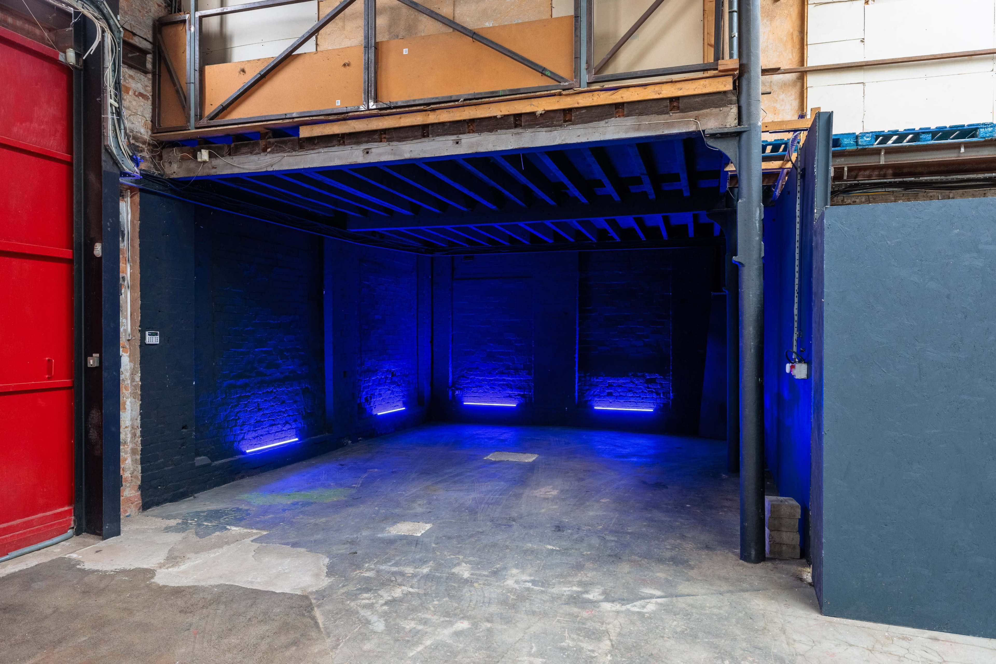 The image shows an empty industrial space with blue LED lights illuminating the walls, and a red door visible on the left.