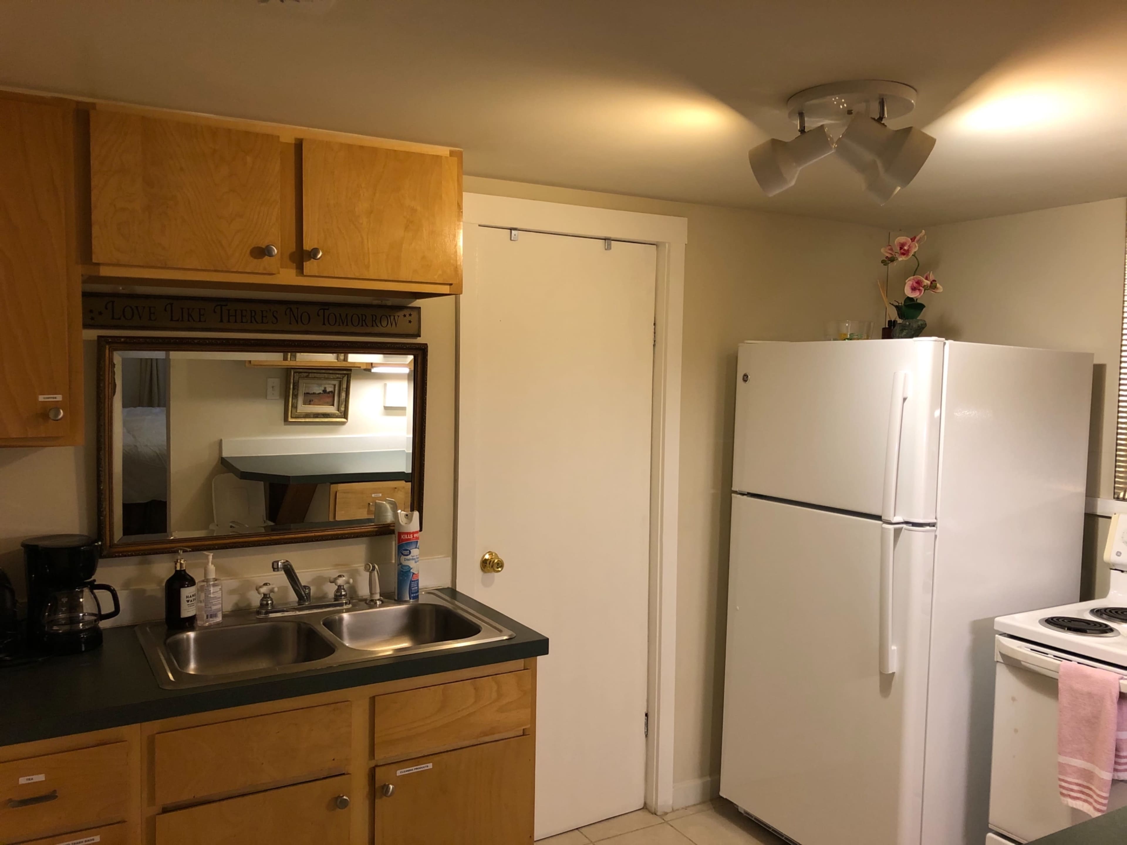 A small kitchen with wooden cabinets, a white refrigerator, a stove, and a mirror on the wall.