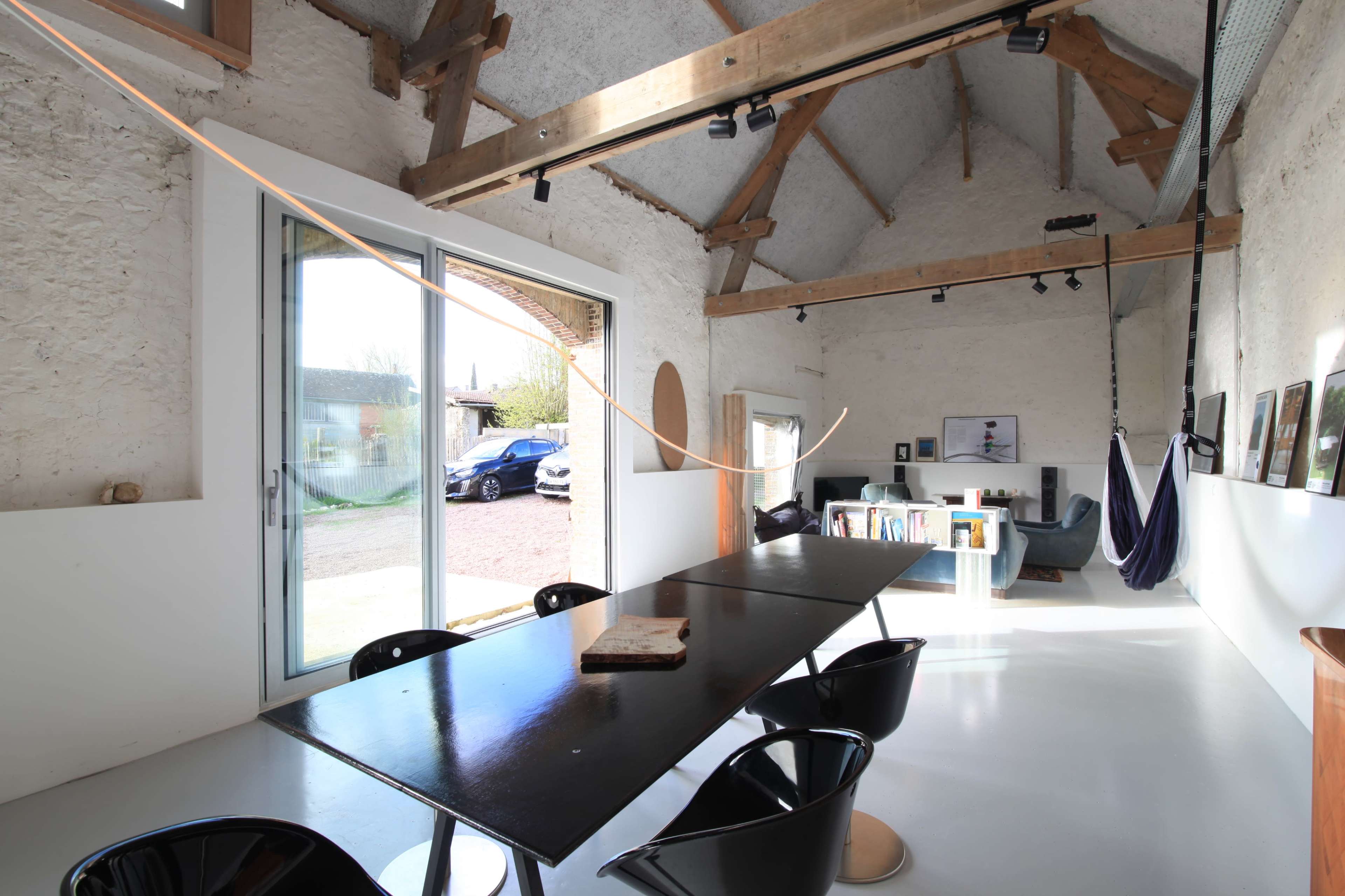 A spacious interior of a modern building with a long black table, chairs, and large windows offering views of the exterior.