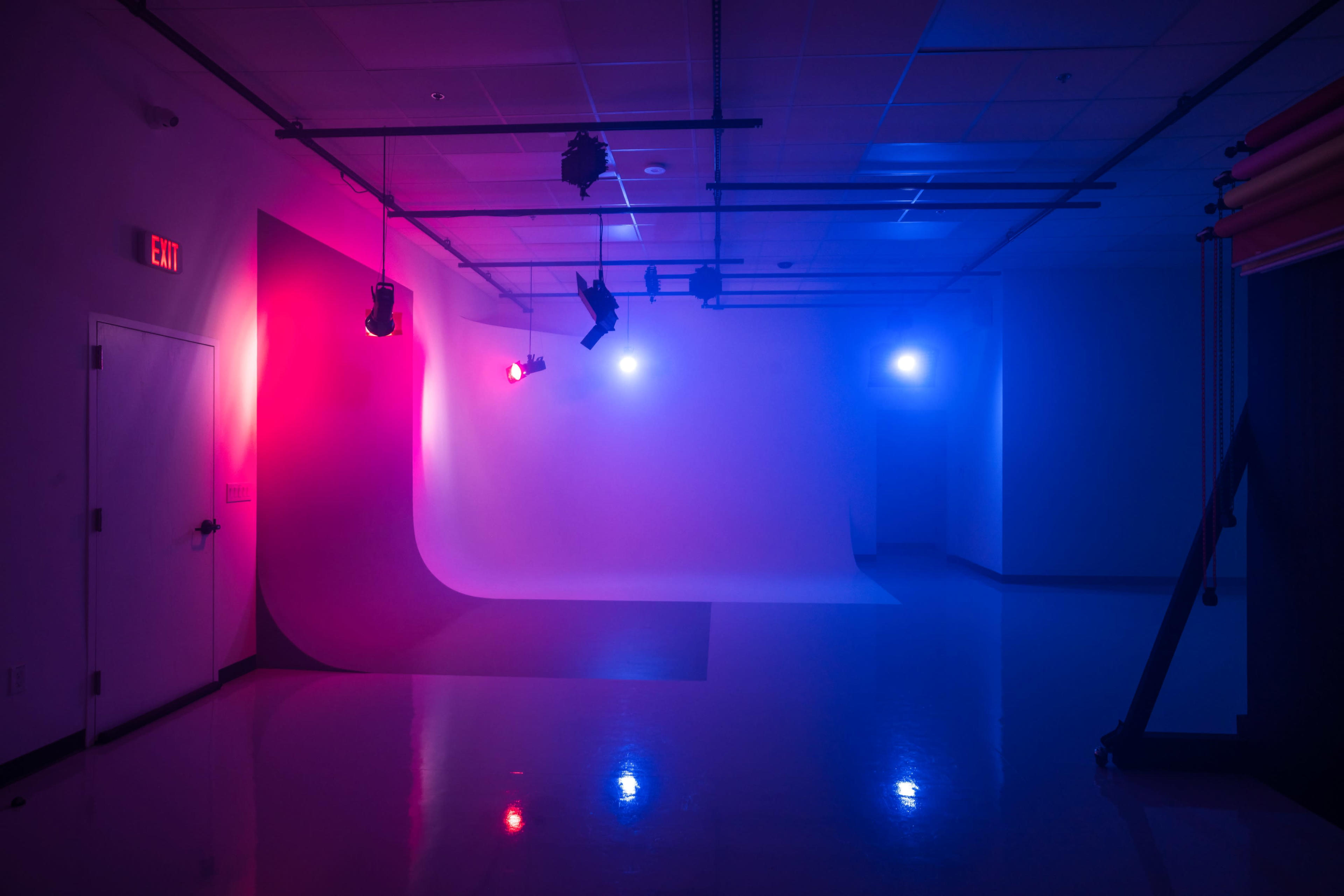 The image shows a photography studio with colored lights illuminating a seamless backdrop and empty floor space.