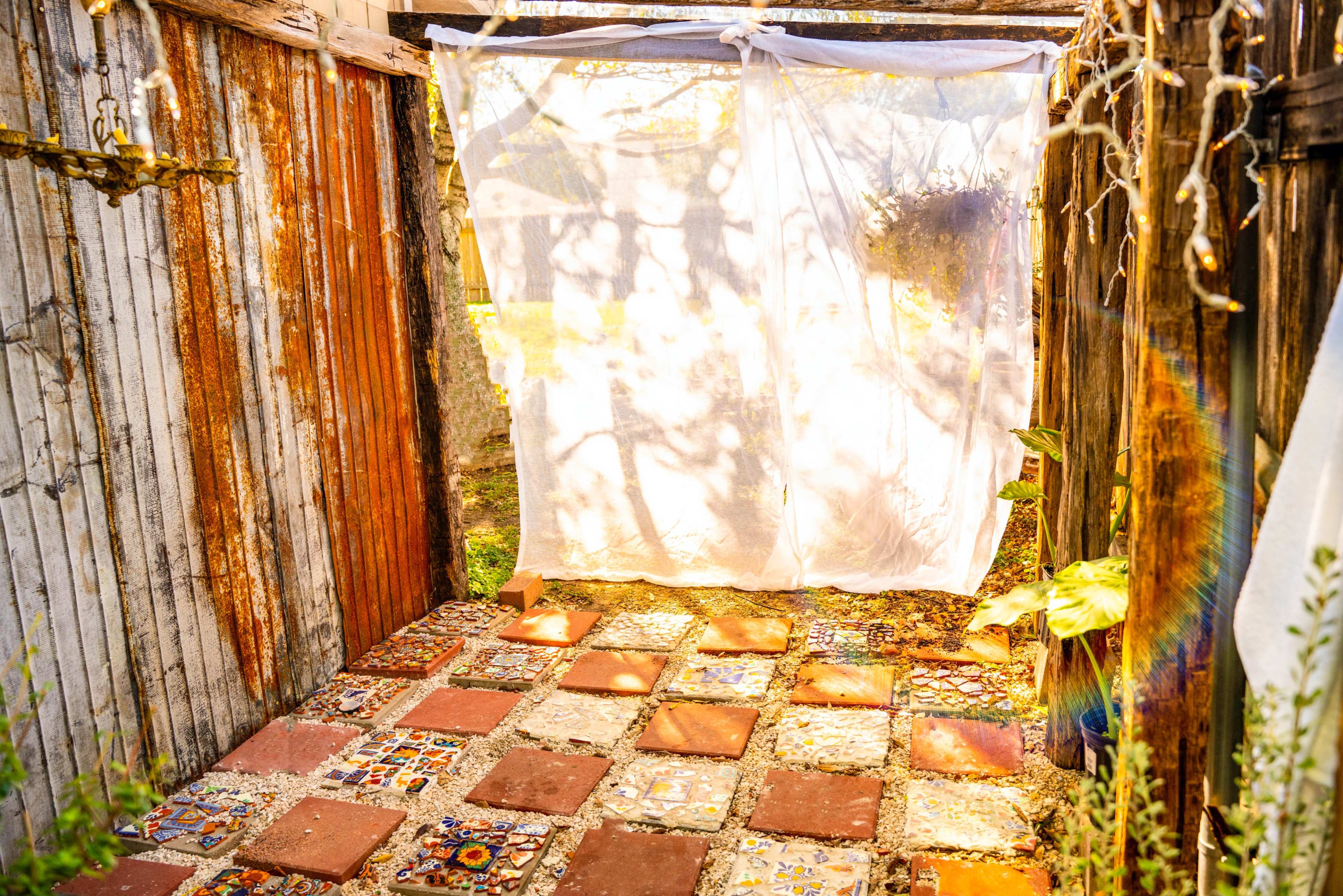 The scene shows a small, outdoor space with a tiled floor and a white fabric curtain hanging in an opening between wooden structures.