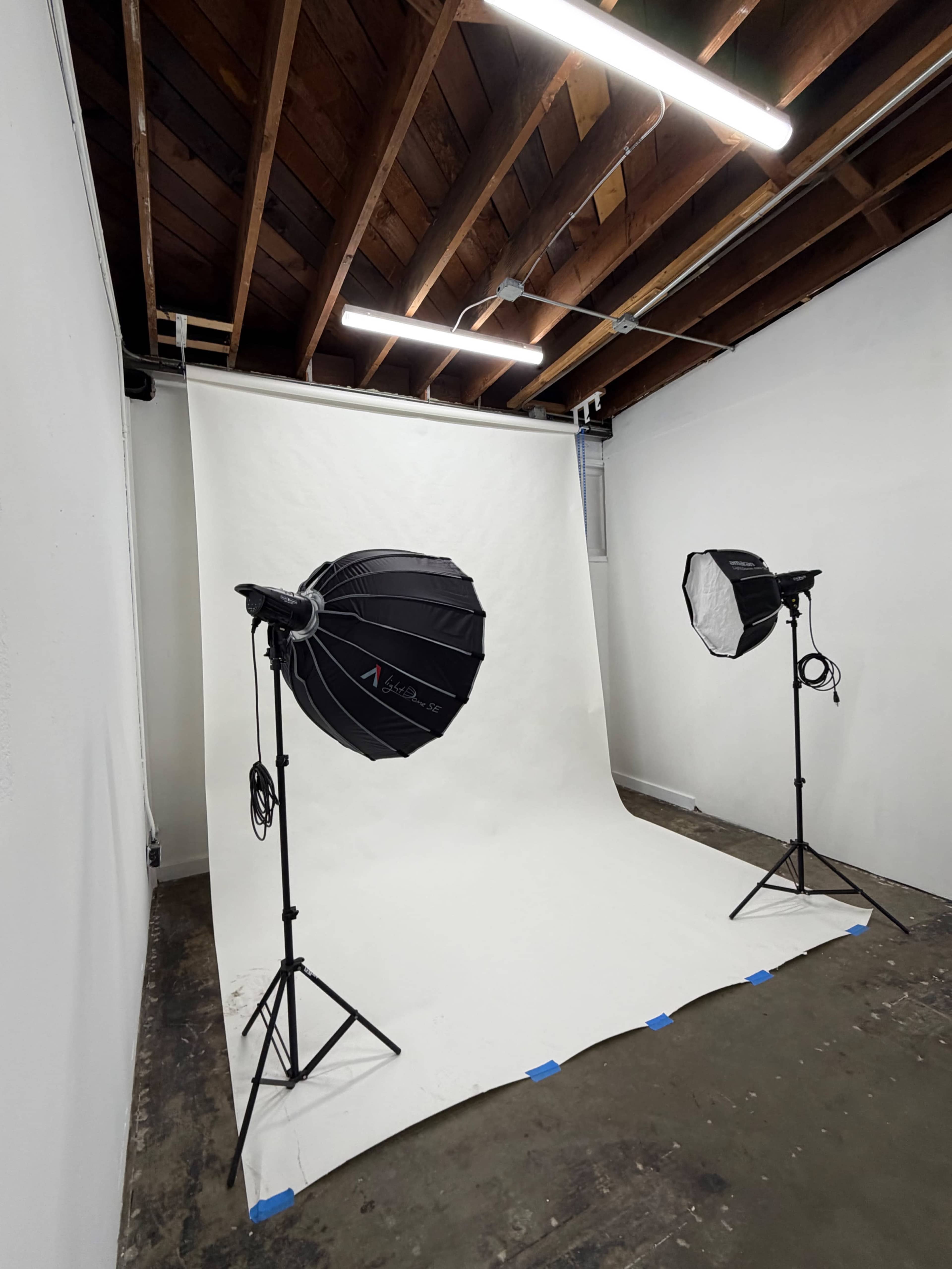 The image shows a photography studio with a white backdrop and two softbox lights positioned on stands on either side.