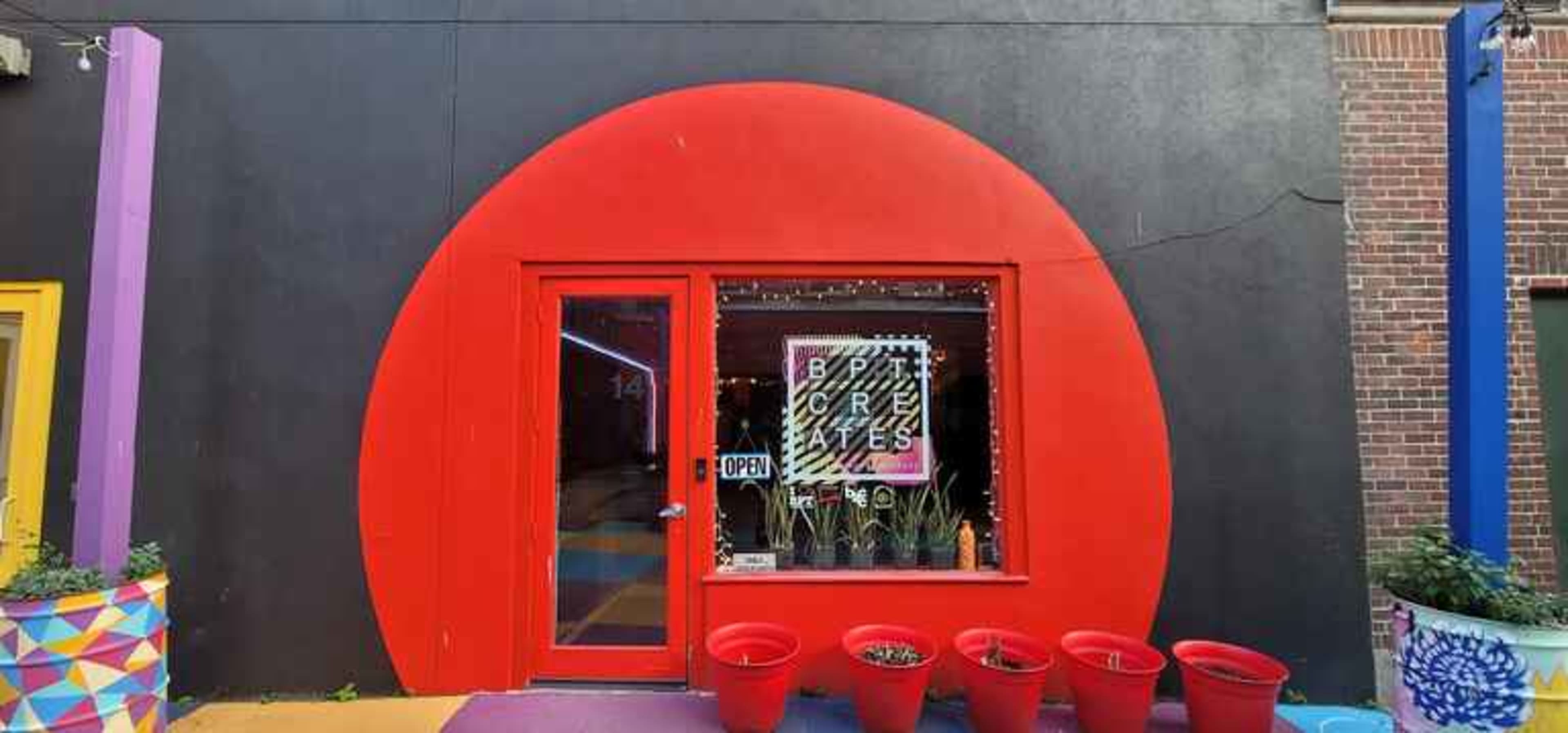 A bright red circular entrance leads to a shop with colorful planters in front.